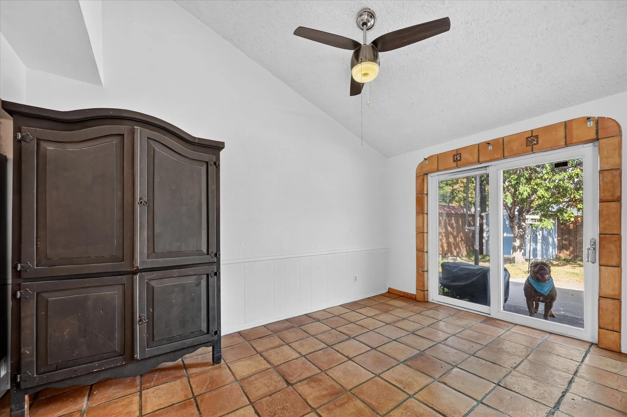 Terracotta-style floor tiling, vaulted ceiling, sliding glass doors, and a ceiling fan with integrated lighting