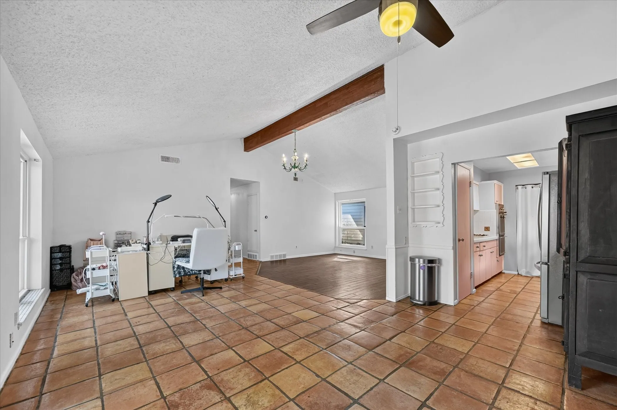 Vaulted ceiling with exposed wood beam, terracotta-style flooring, and a ceiling fan