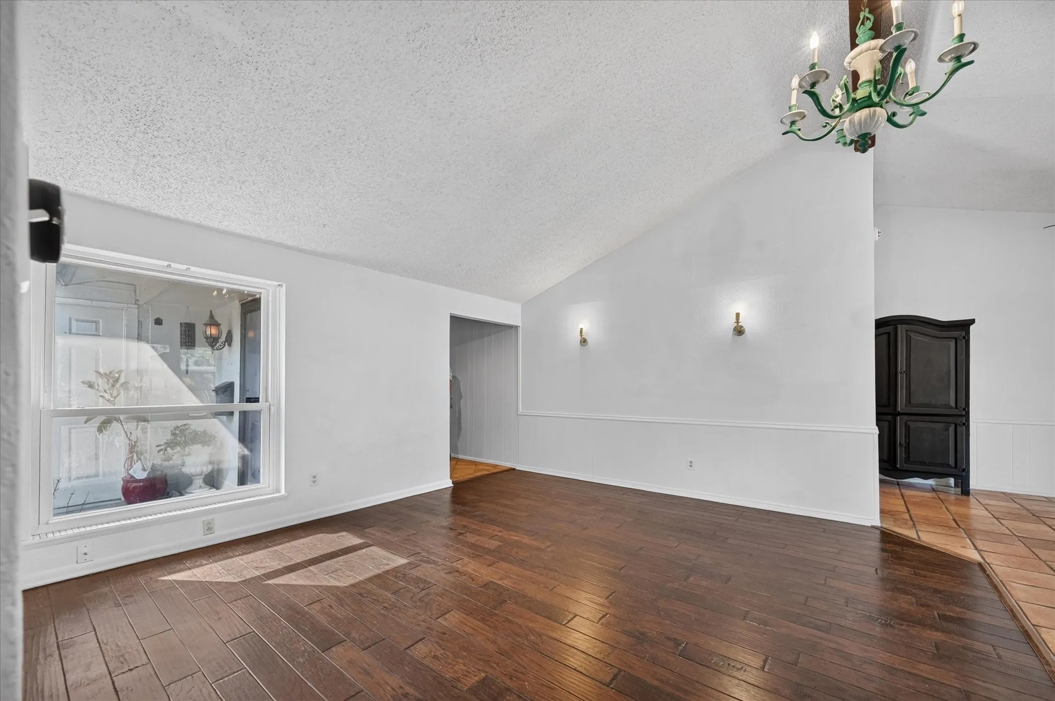 Vaulted ceiling, wood-finish flooring, white walls, picture window, and chandelier