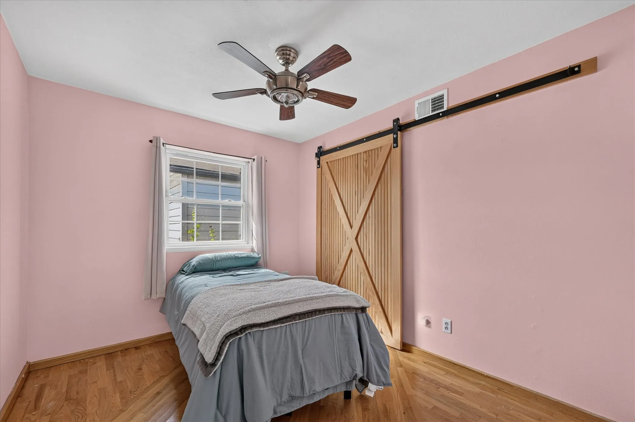 Wood-finish flooring, single window, wood barn door, and a ceiling fan with light