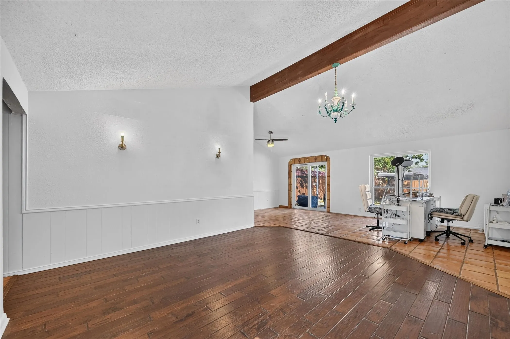 Vaulted ceiling with exposed wood beam, wood-finish flooring, wainscoting, and large windows