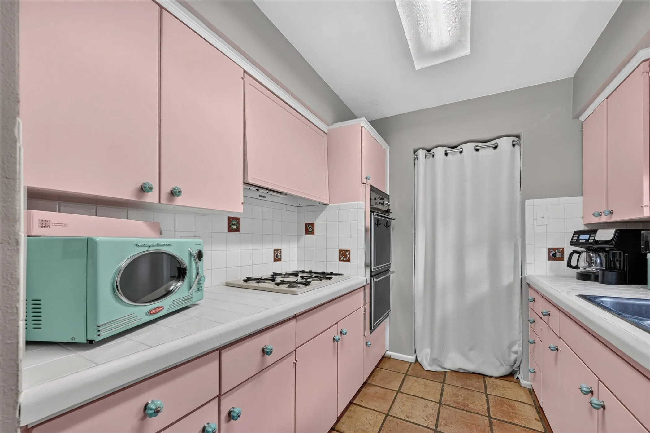 Galley kitchen with pink cabinetry, tile flooring, tile countertops, and a double wall oven