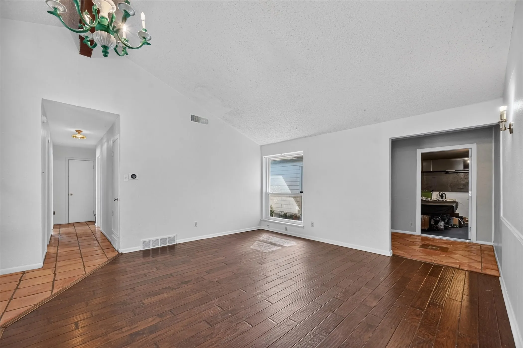 Vaulted ceiling, wood-finish flooring, single window, and a decorative chandelier