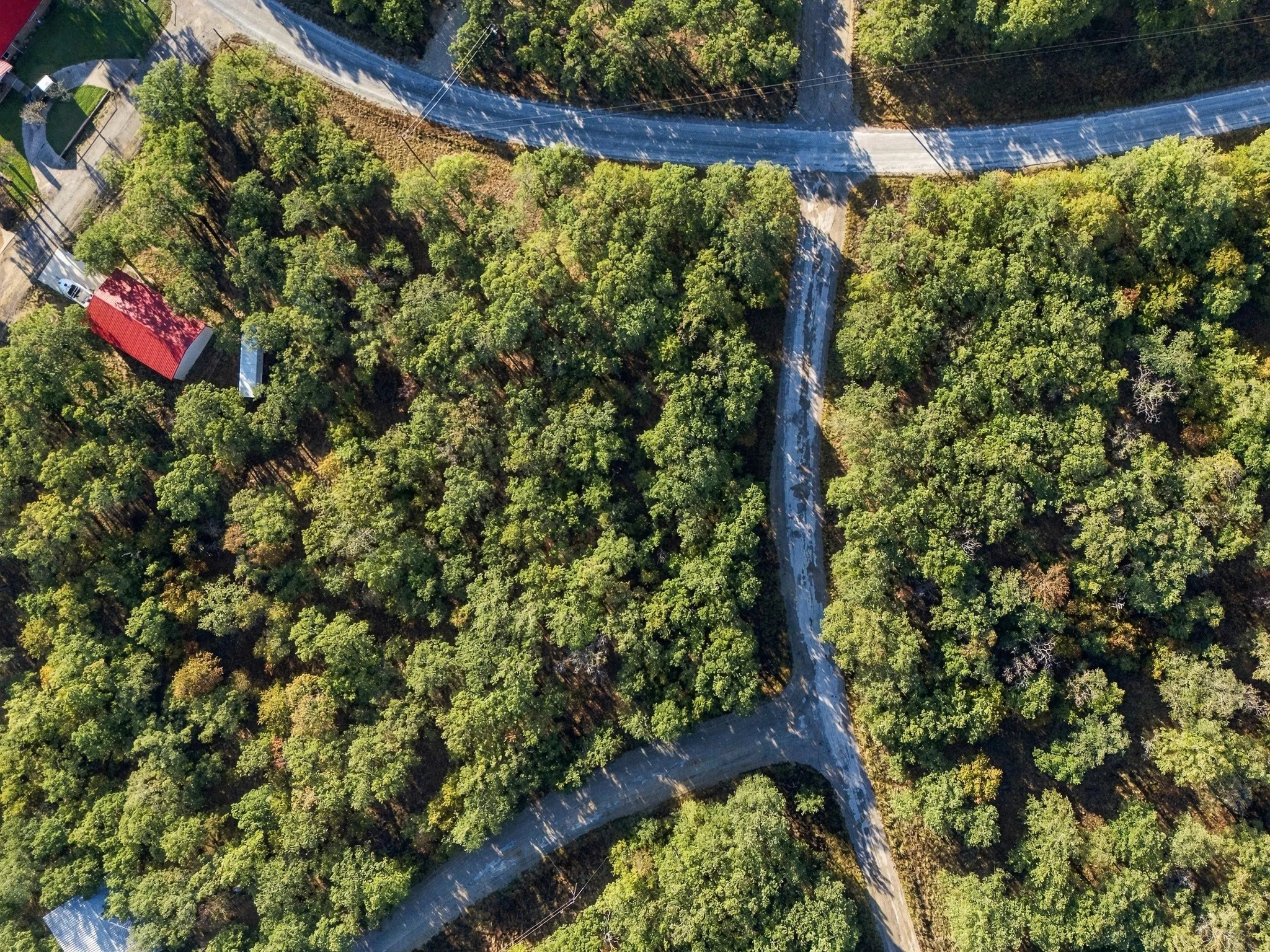 Wooded acreage featuring multiple roads, a red-roofed structure, and a white rectangular structure
