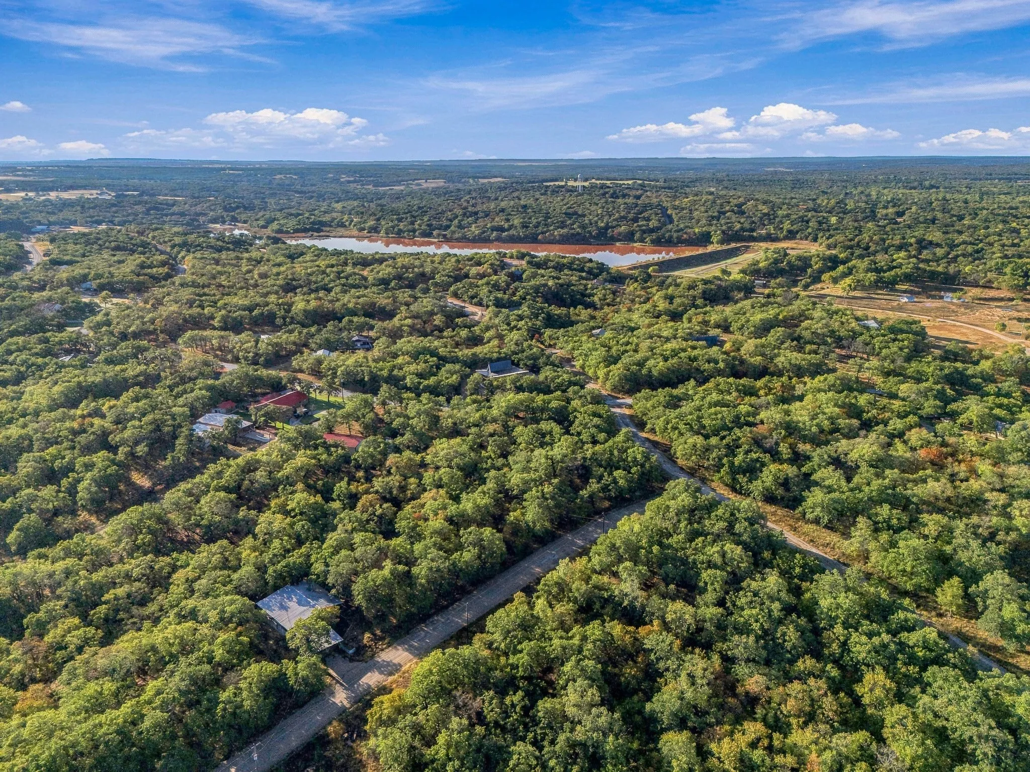 Expansive natural landscape featuring a large body of water, dense tree coverage, and a clear blue sky