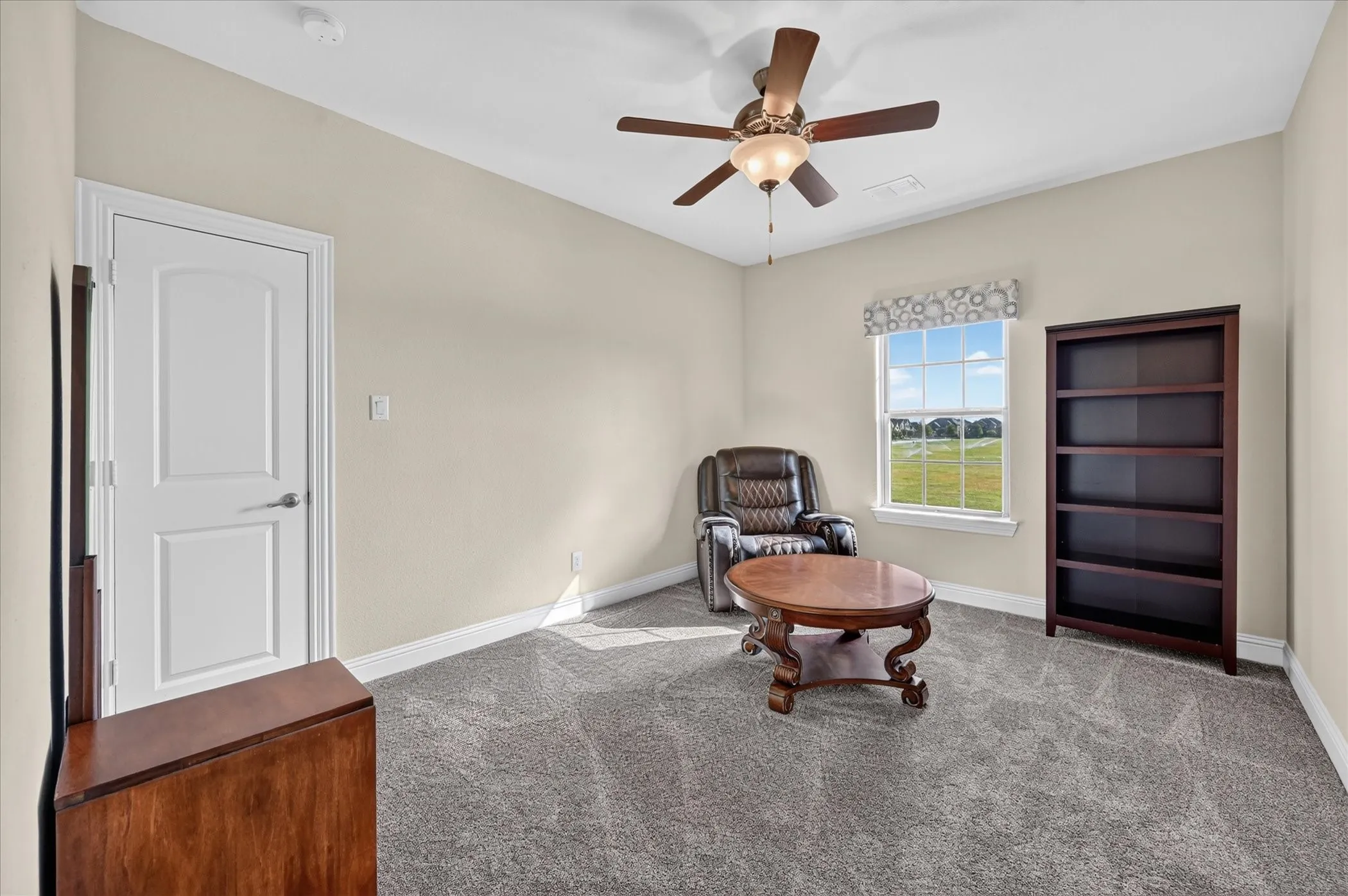 Carpeted room featuring a ceiling fan with light fixture, a window with a patterned valance, and a white interior door