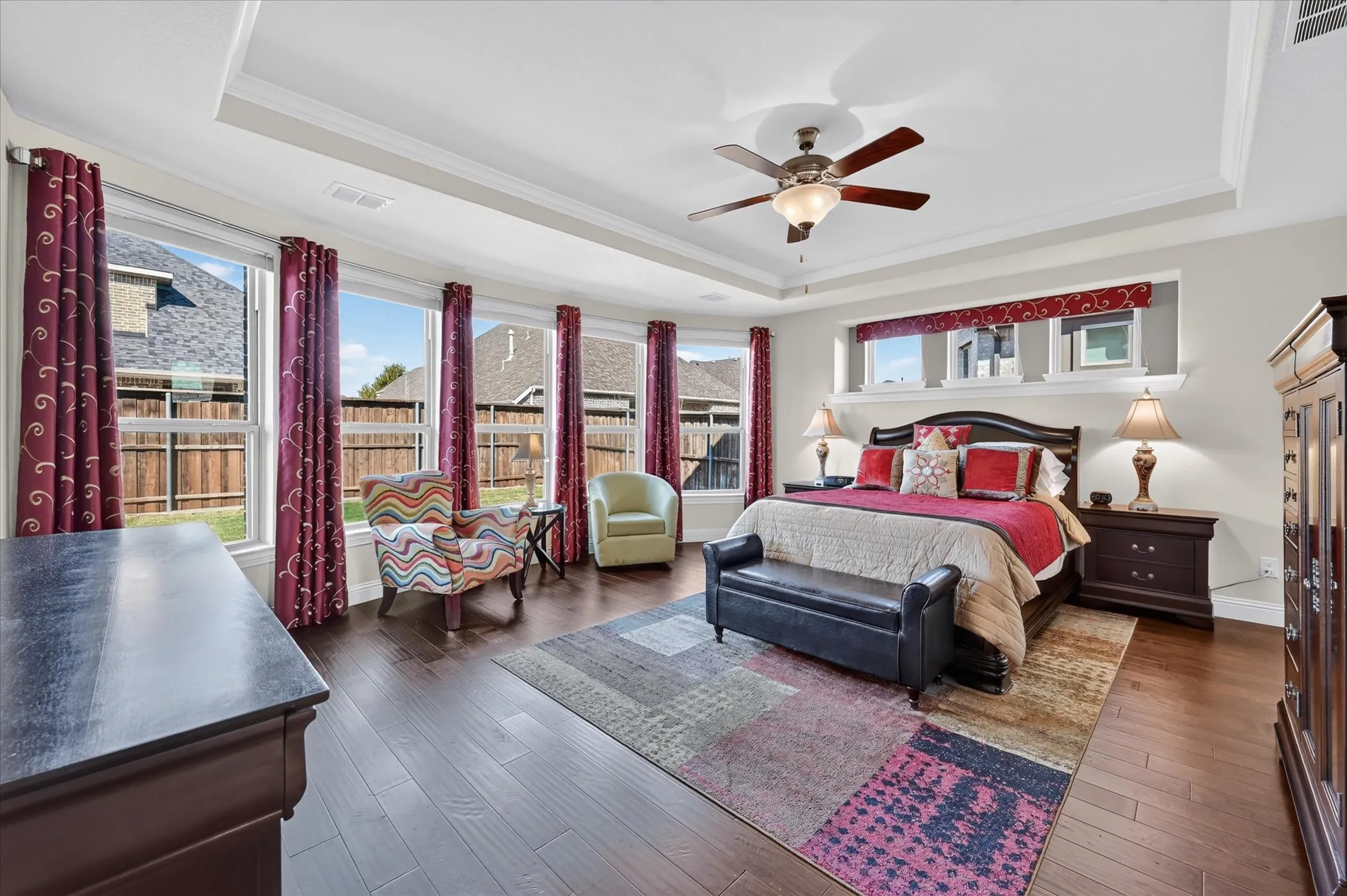 Tray ceiling with crown molding, ceiling fan, wood-finish flooring, and multiple windows