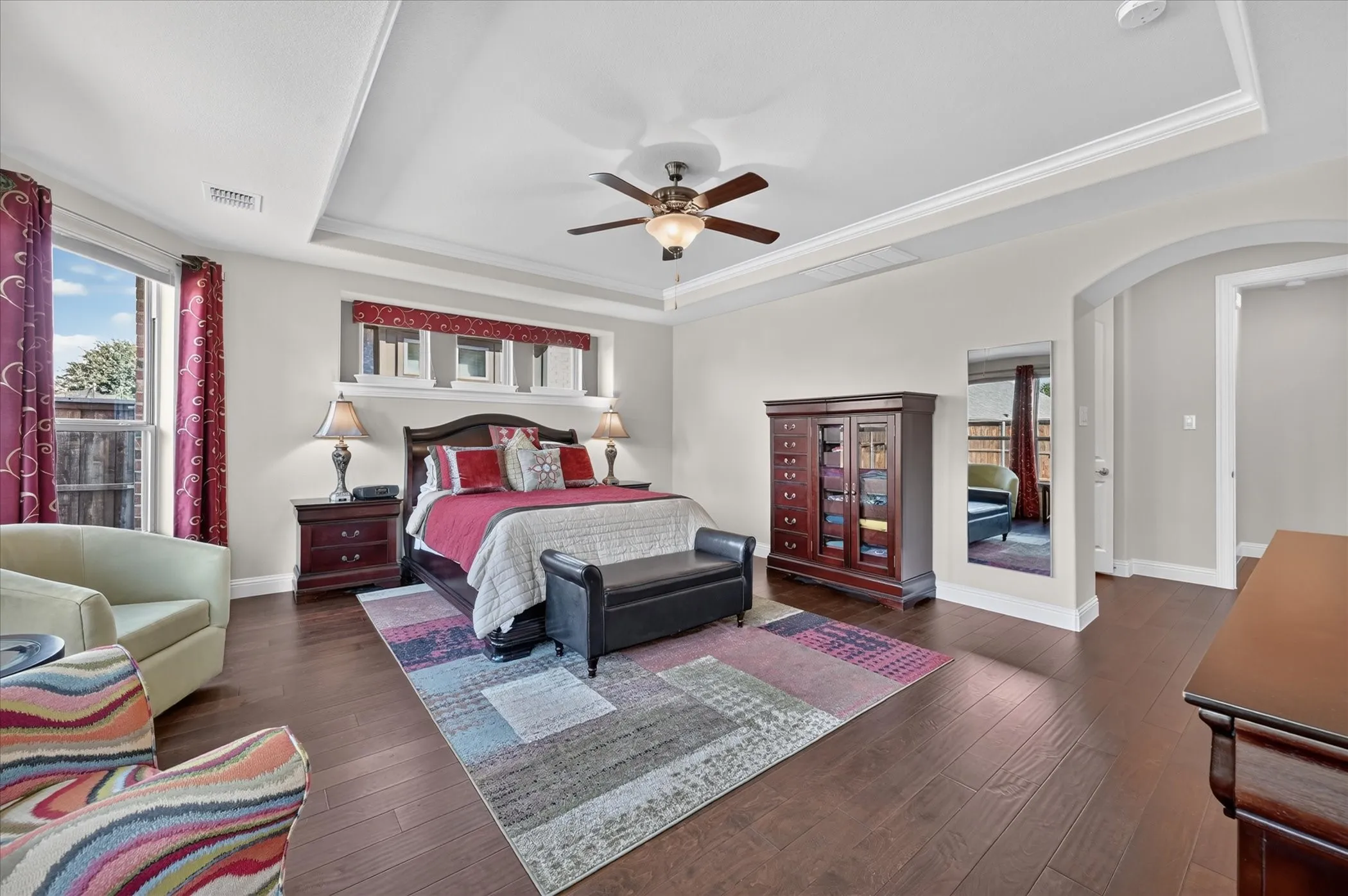 Tray ceiling with a ceiling fan, wood-finish flooring, arched doorway, and multiple windows
