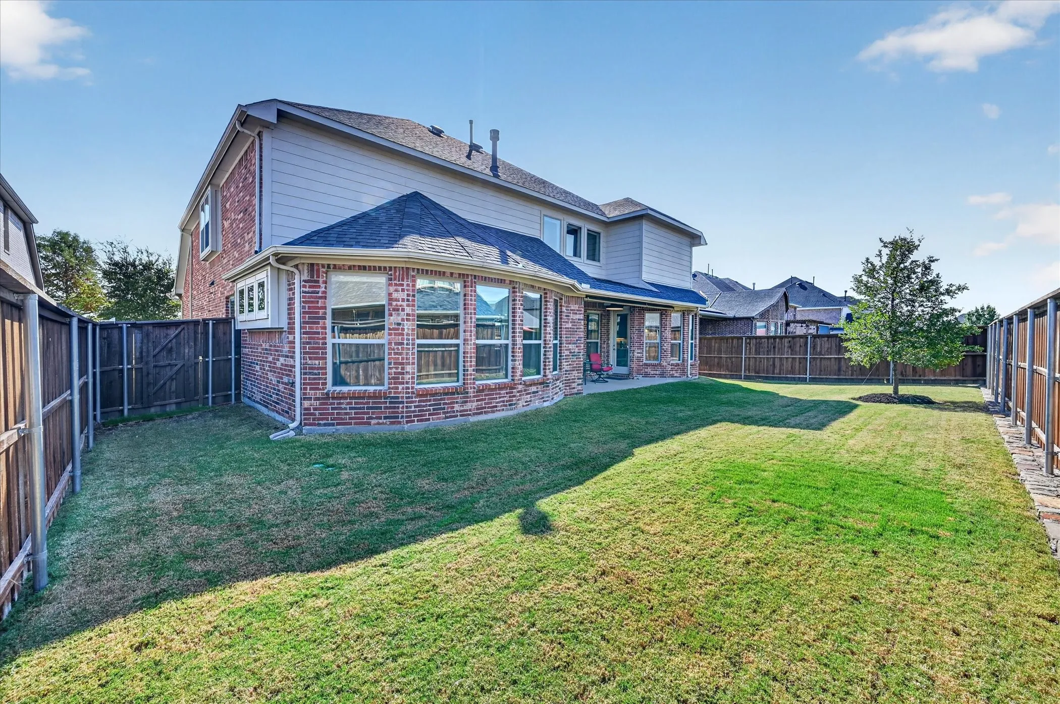 Expansive backyard featuring a manicured lawn, full privacy fencing, and a mature tree