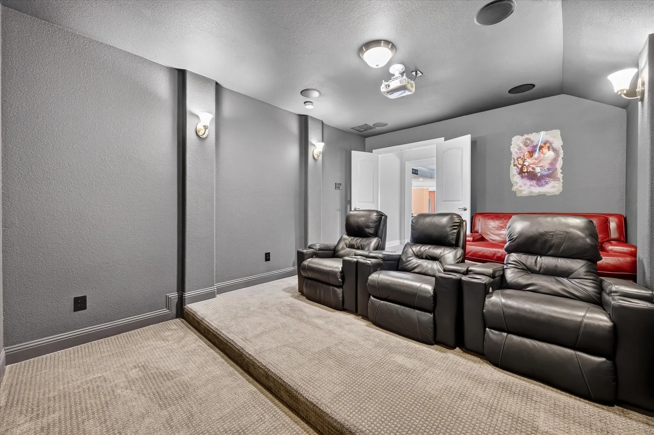 Dedicated media room featuring tiered carpeting, recessed lighting, and wall sconces
