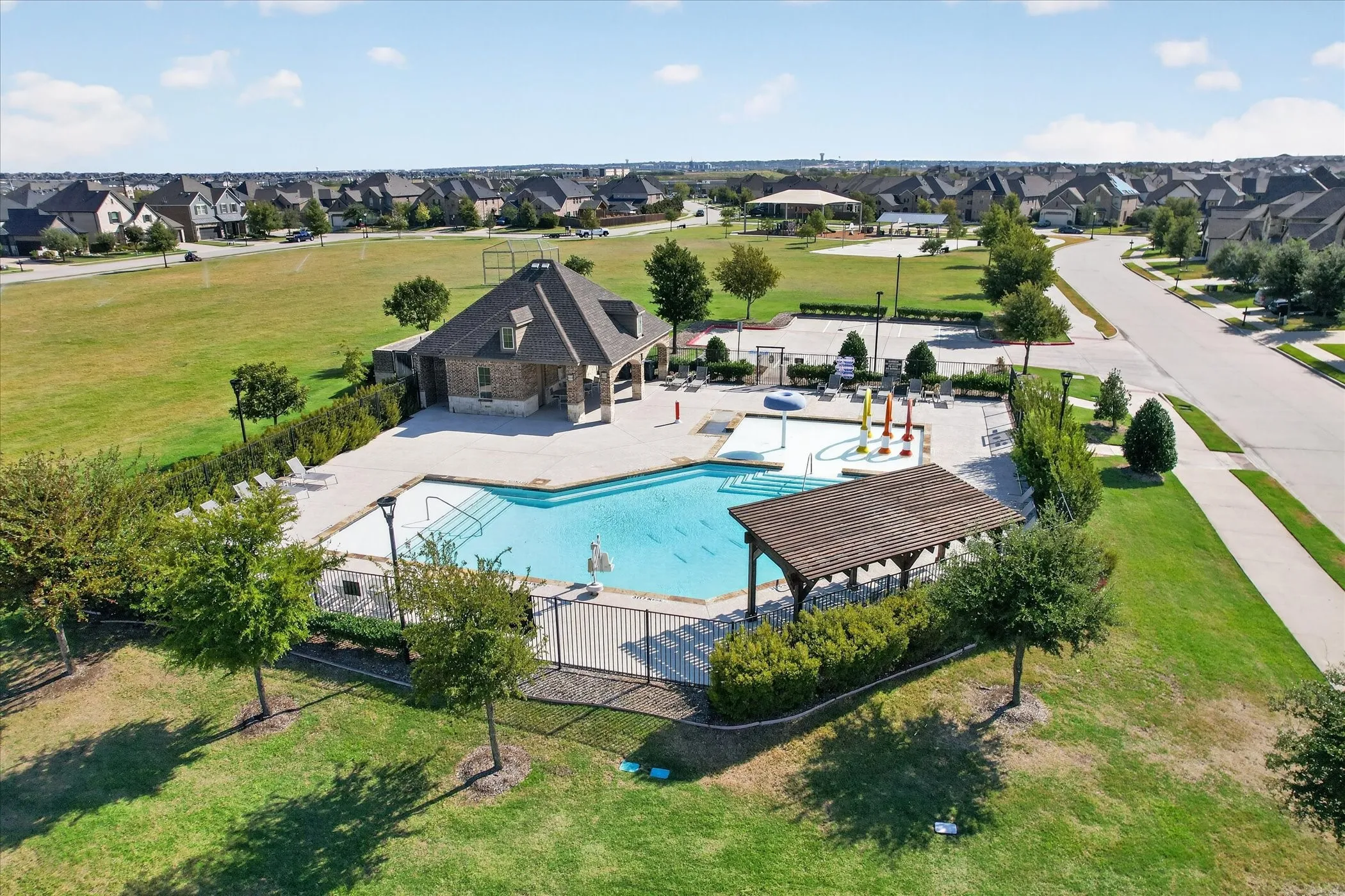 Community swimming pool with a covered pergola, adjacent splash pad, and a clubhouse building