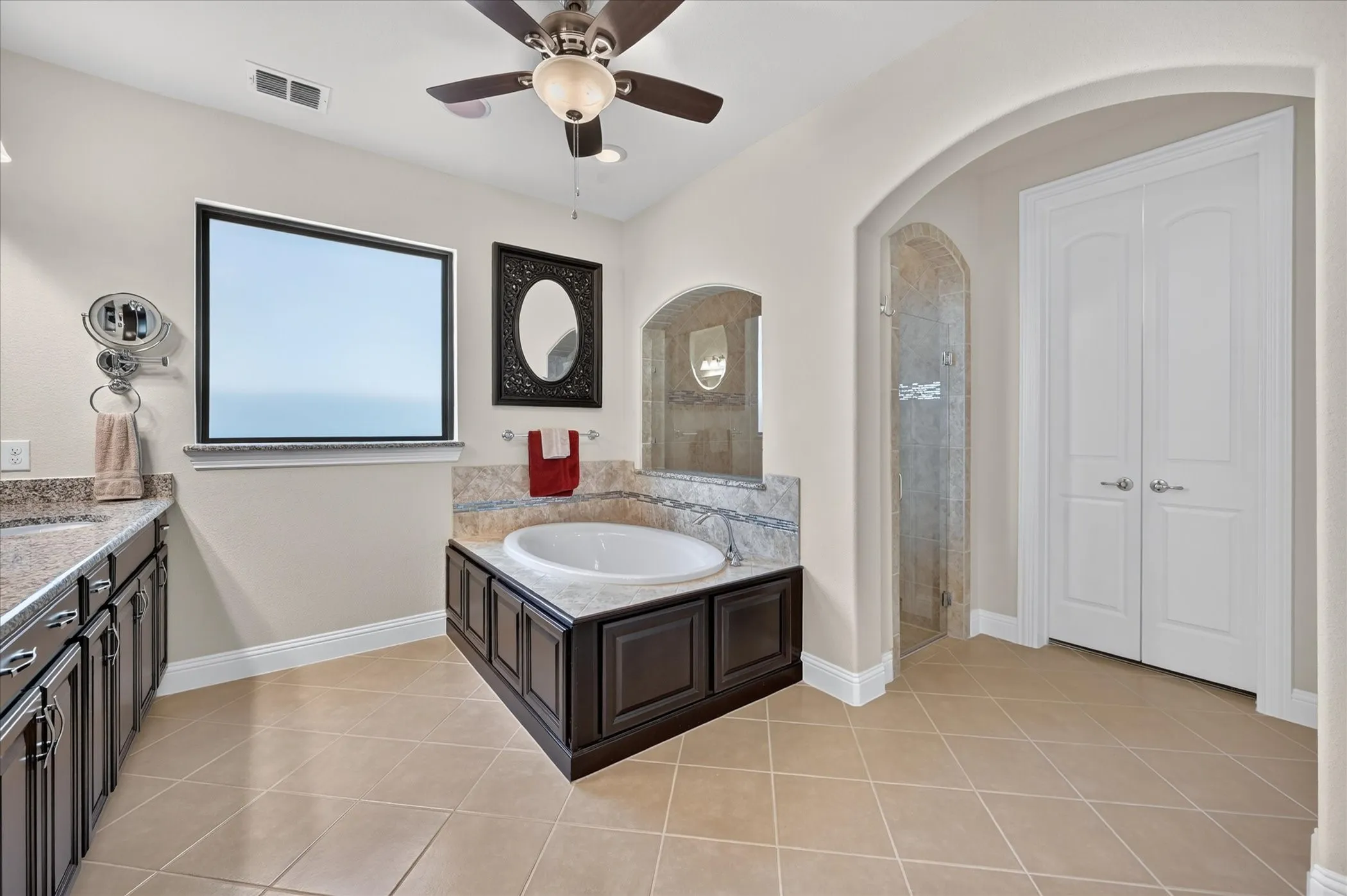 Built-in soaking tub, dual vanity with stone countertops, arched doorway, tiled shower, and tiled flooring