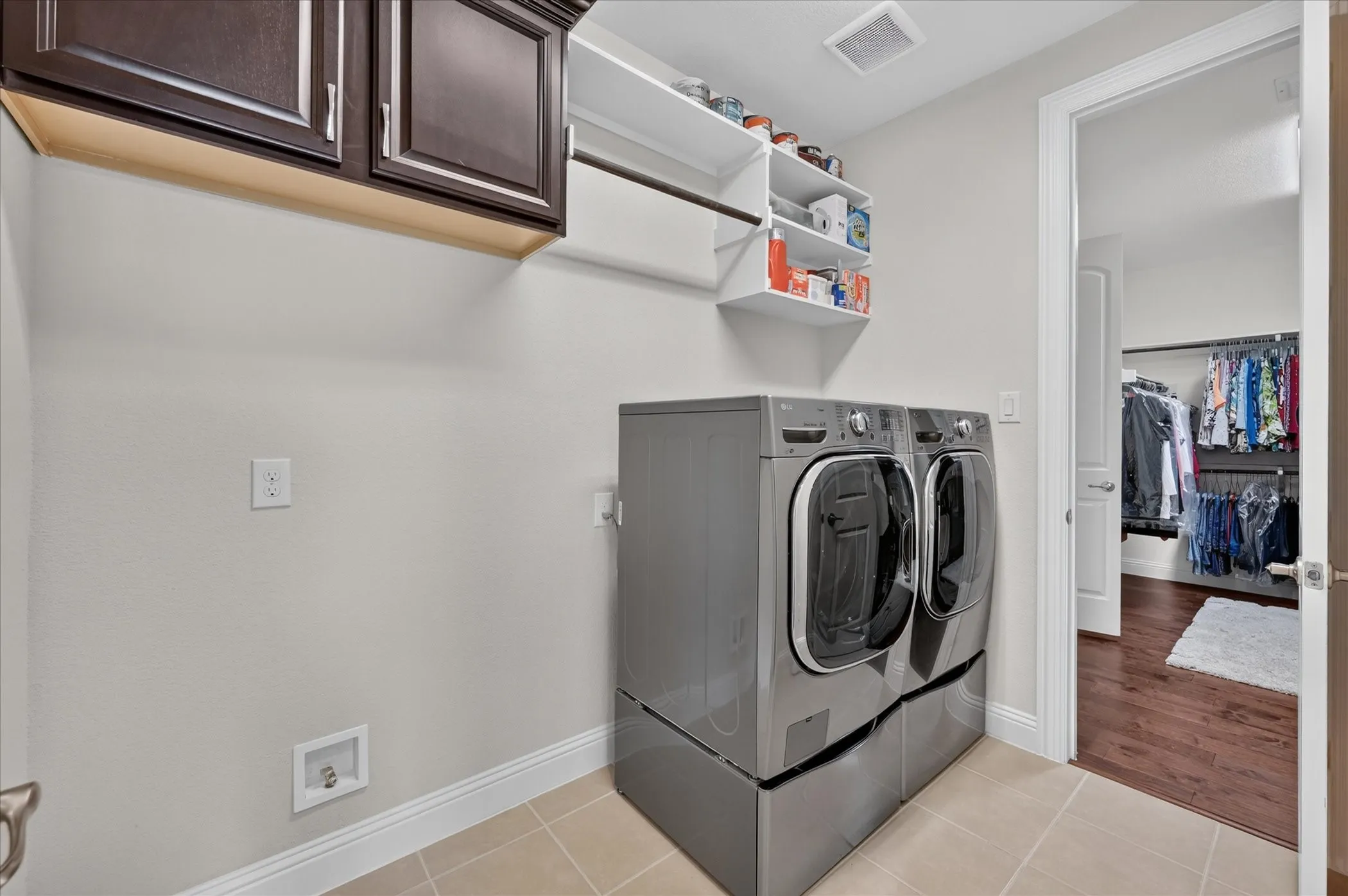 Laundry area featuring dark wood-finish cabinetry, open shelving, and light-toned tile flooring