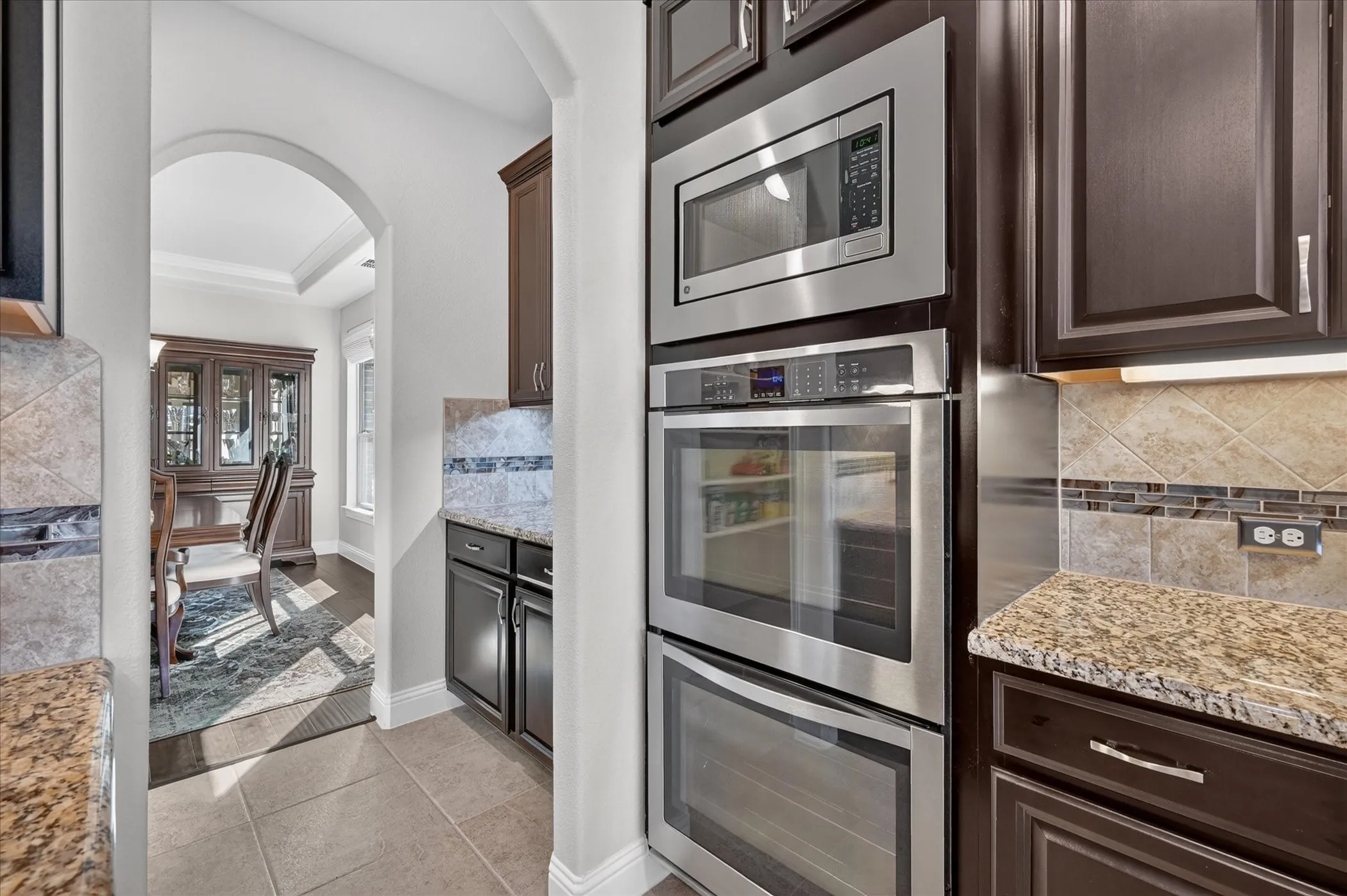 Built-in stainless steel double ovens, rich wood-finish cabinetry, granite countertops, and tiled backsplash