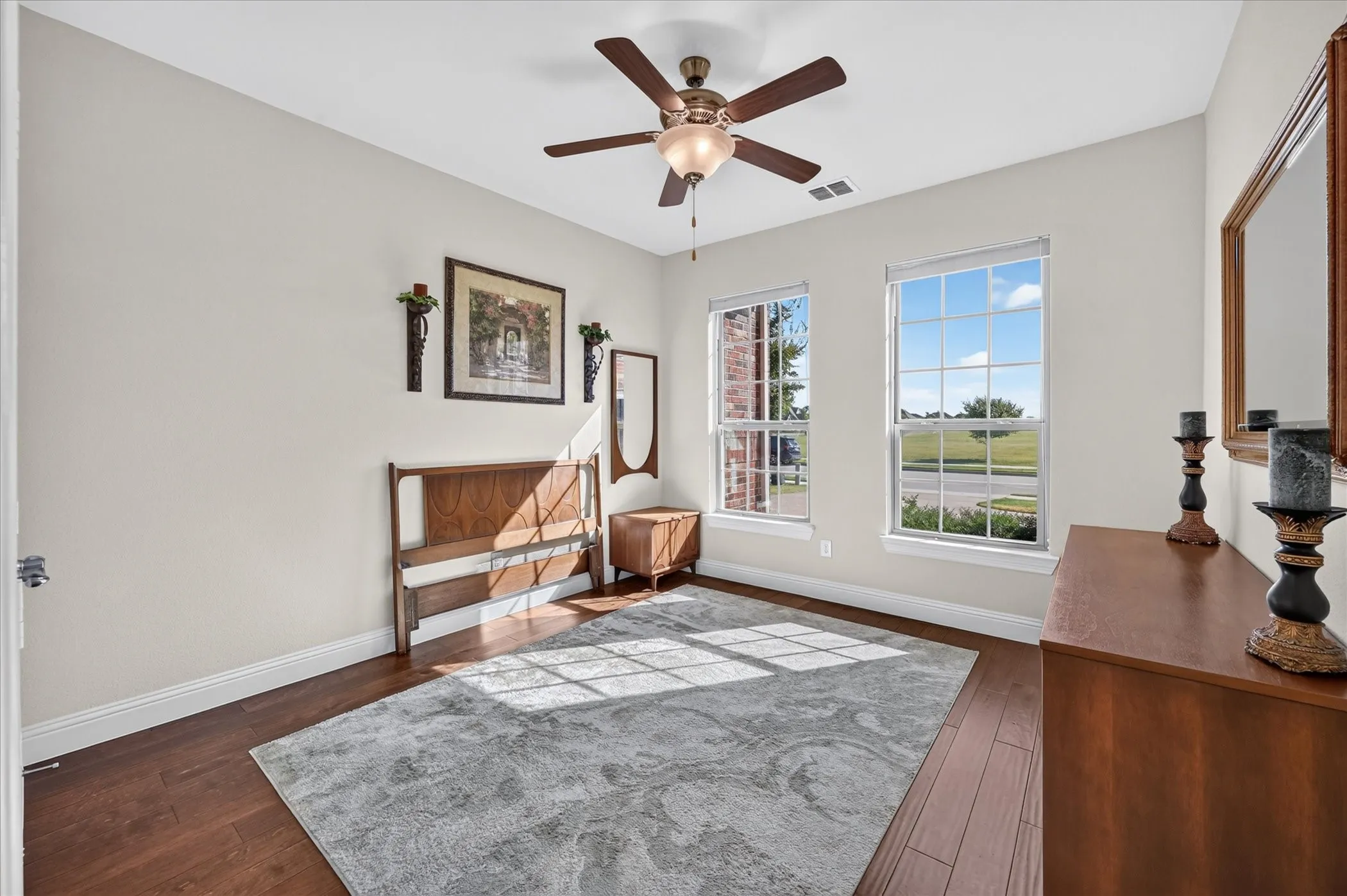 Hardwood-style flooring, two large windows, a ceiling fan with integrated lighting, and neutral wall tones