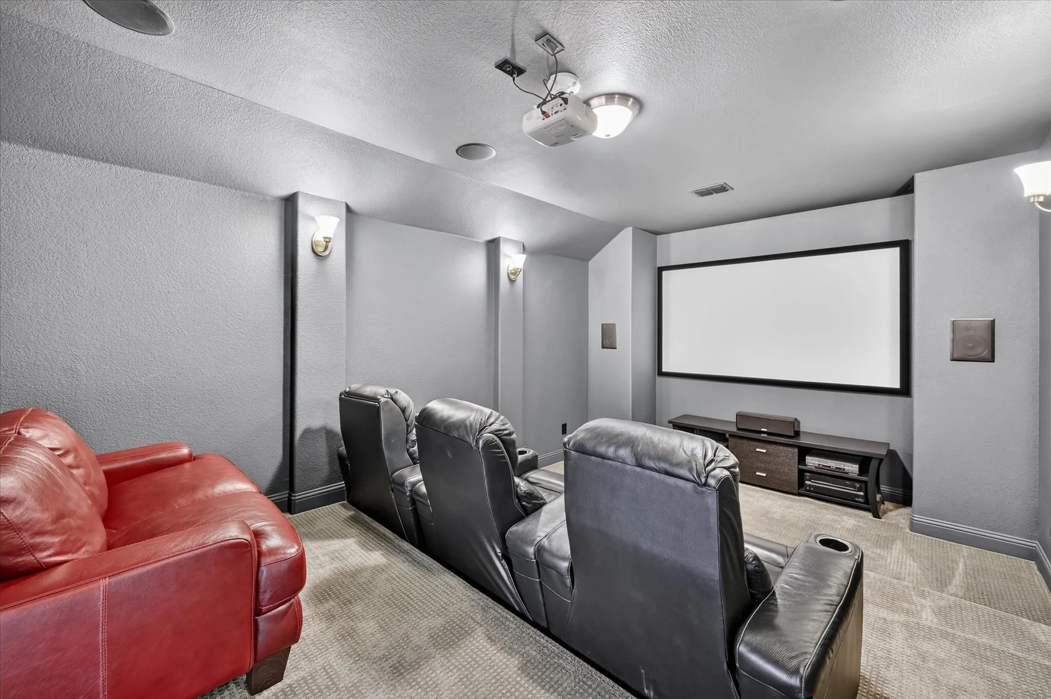Dedicated media room featuring a large projection screen, wall-mounted speakers, recessed ceiling lighting, and sconce lighting