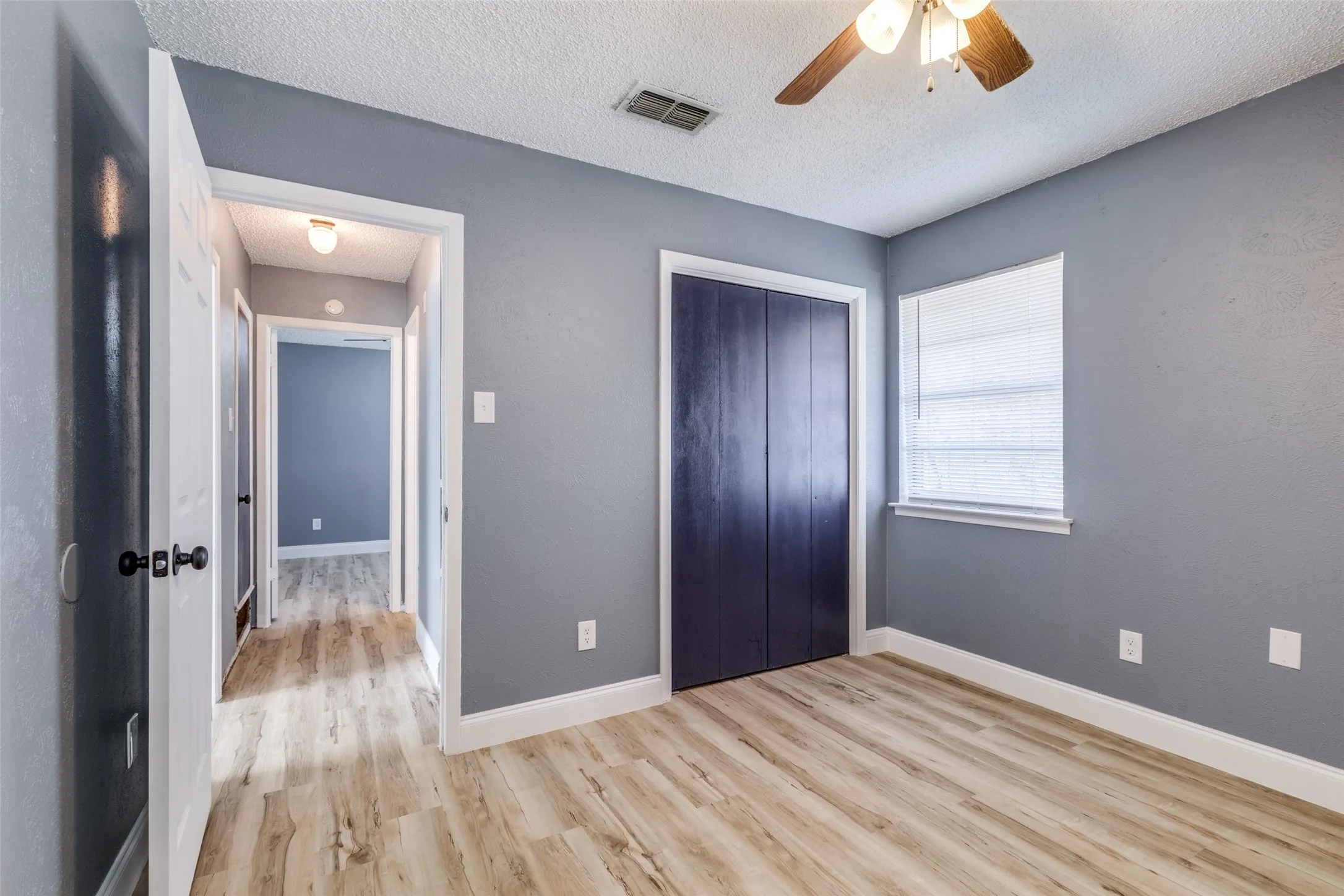 Wood-finish flooring, ceiling fan, white trim, and a window with blinds