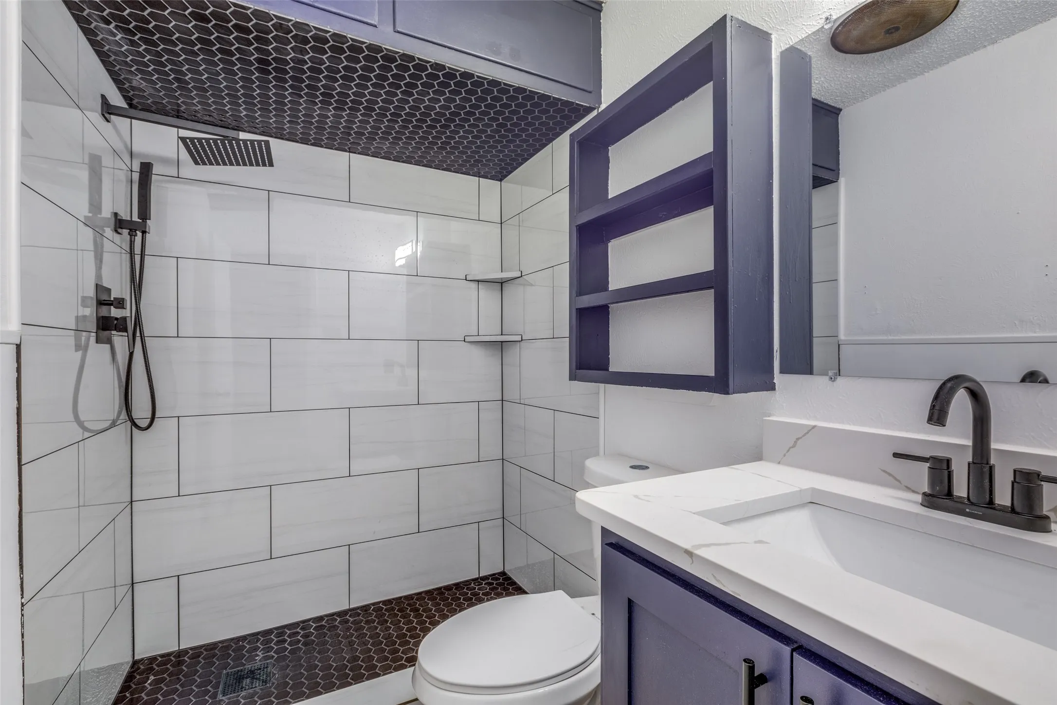White subway tile shower with a dark hex tile floor and ceiling accent