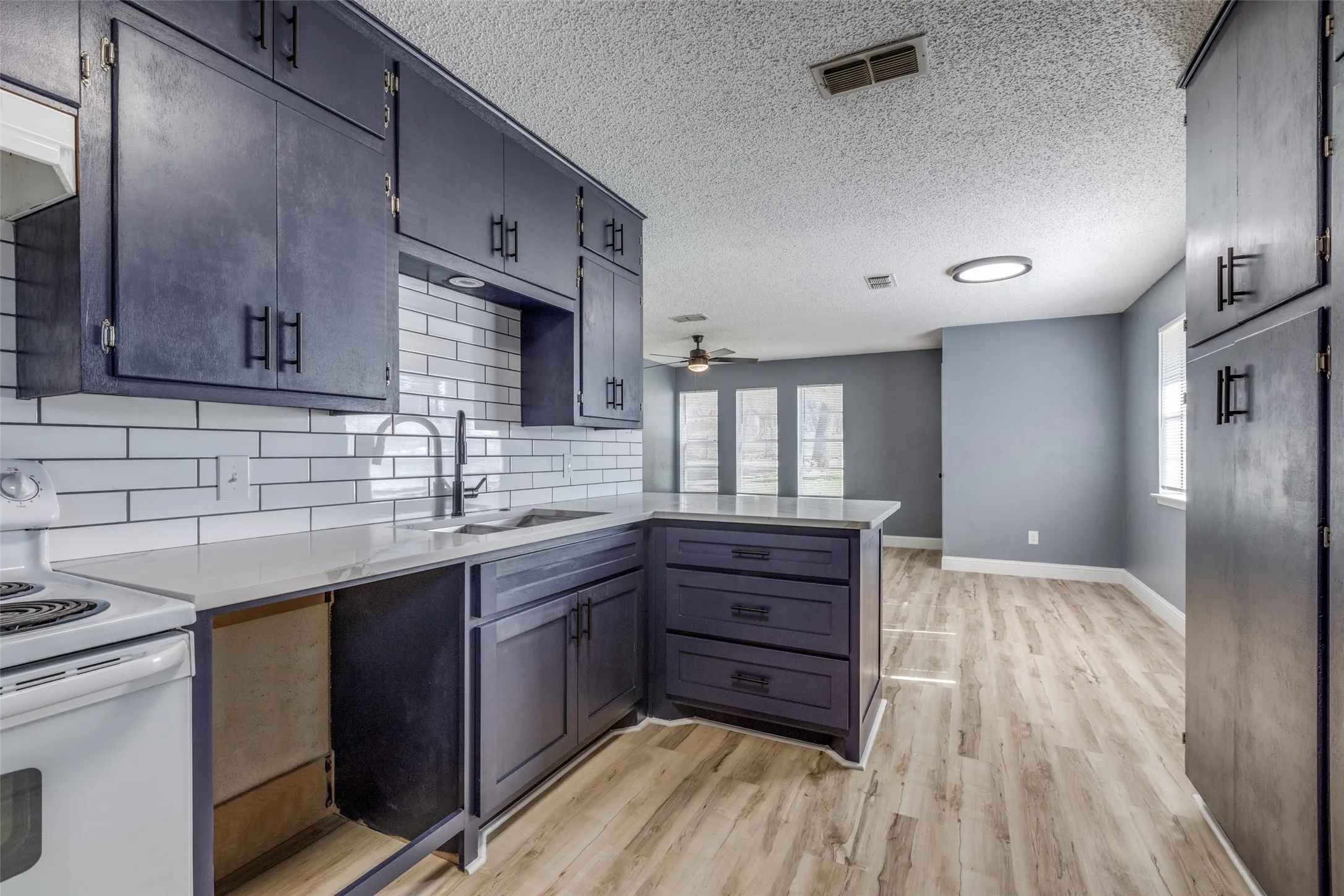Kitchen featuring dark cabinetry, white subway tile backsplash, light countertops, and wood-finish flooring