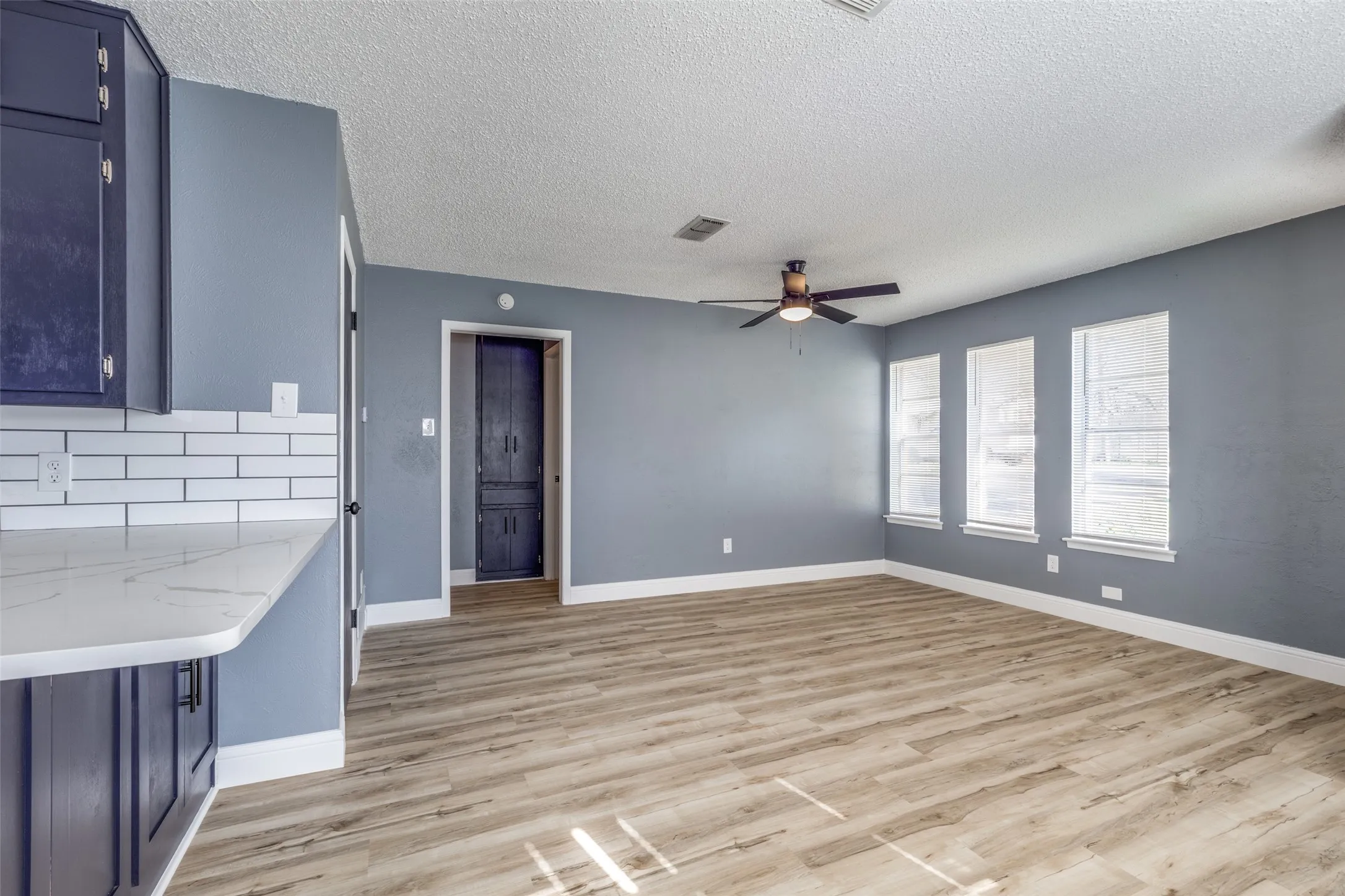 Wood-finish flooring, white subway tile backsplash, white quartz-finish countertop, dark wood cabinetry, and a ceiling fan