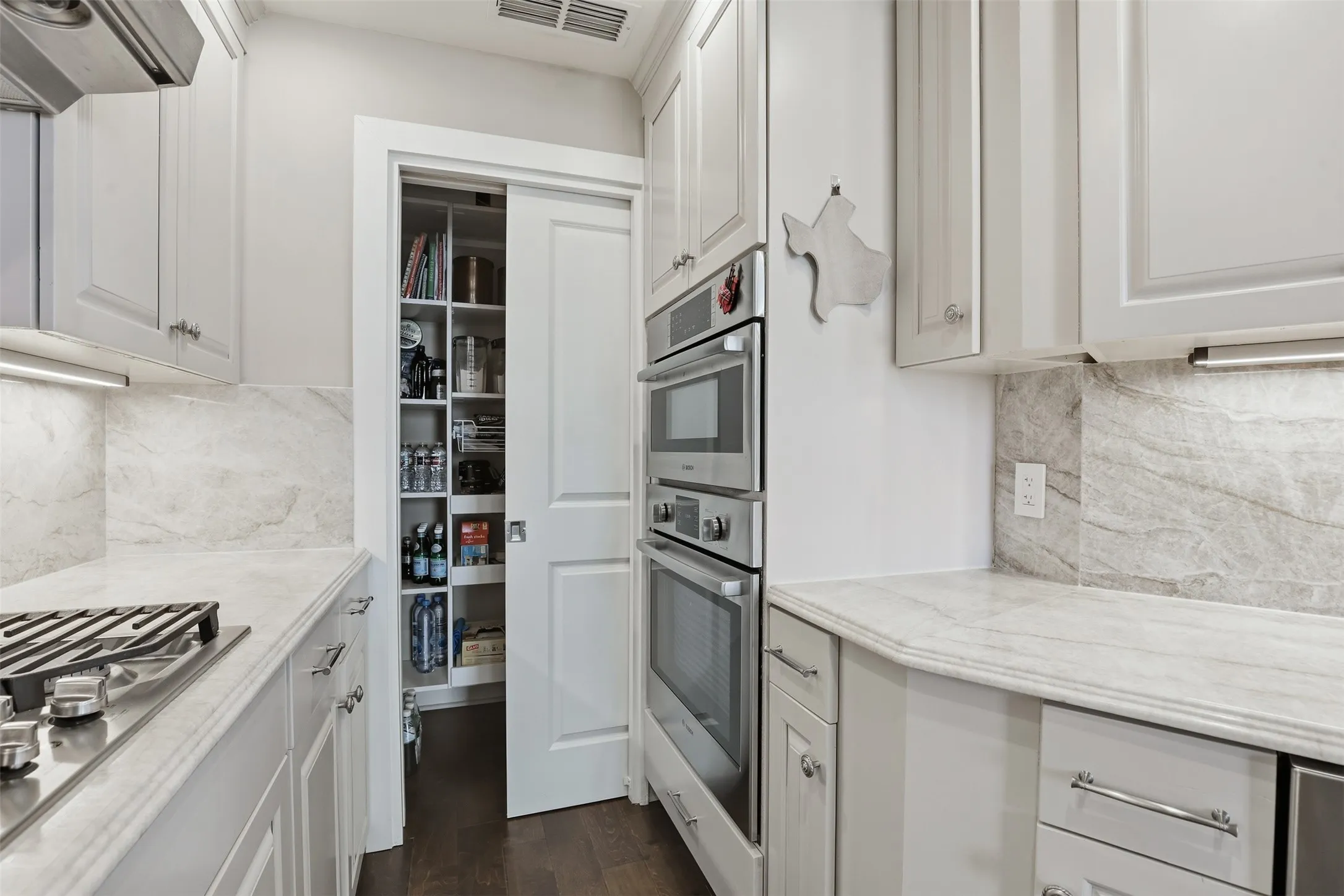 Kitchen featuring light-toned cabinetry, slab countertops, a gas cooktop, built-in double ovens, and a walk-in pantry