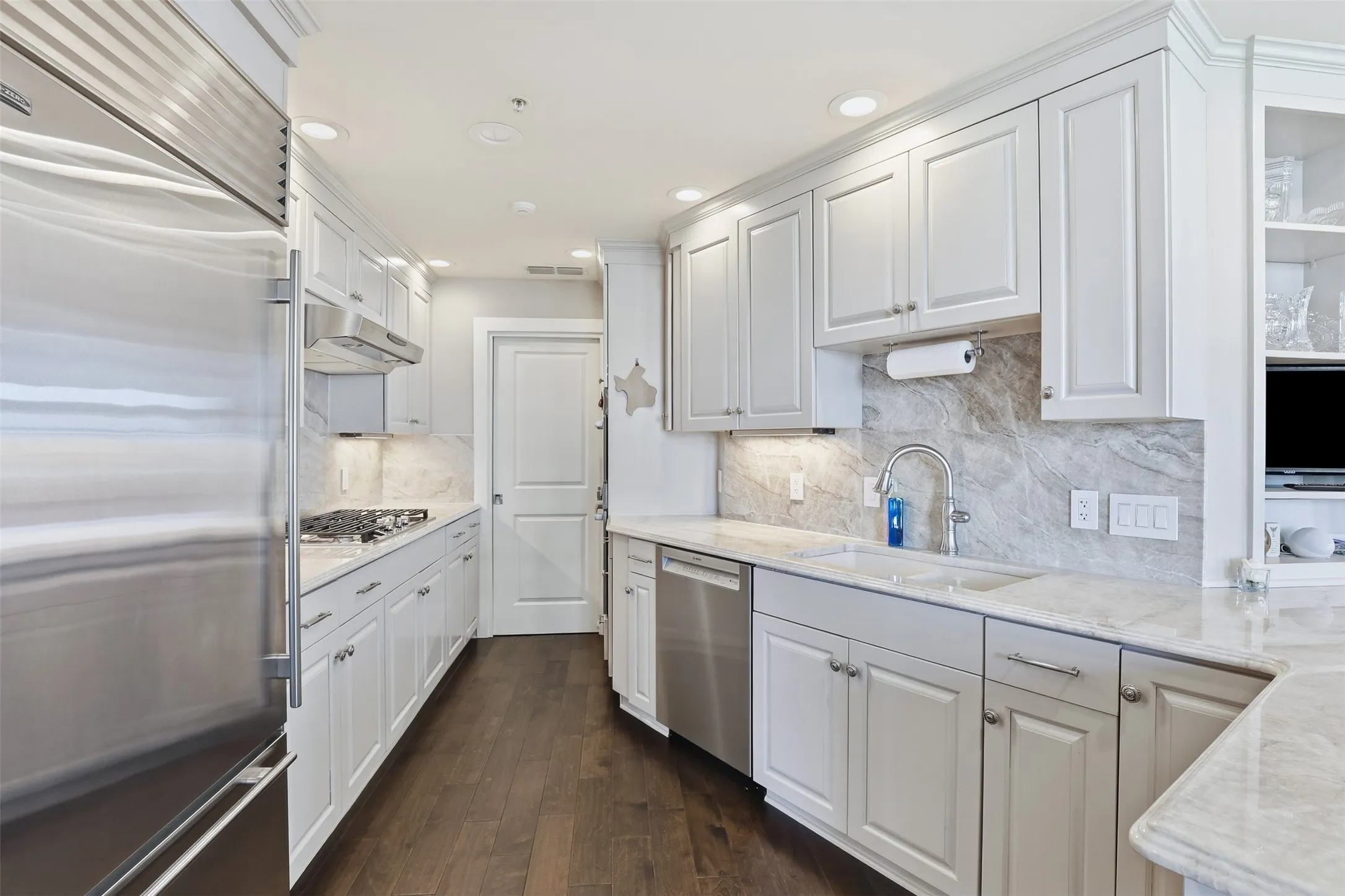 Gourmet kitchen featuring stainless steel appliances, white cabinetry, stone countertops, and wood-finish flooring