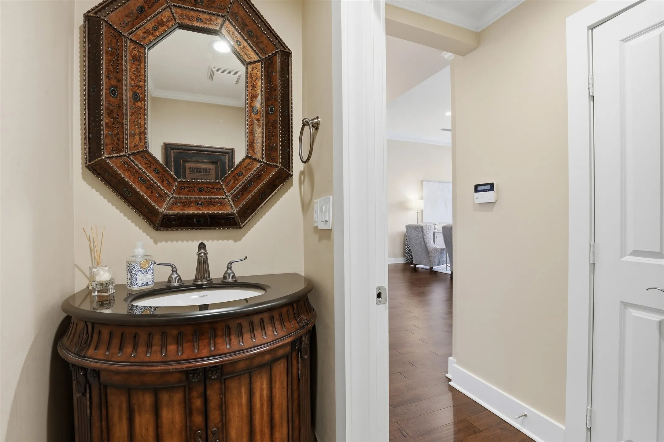 Ornate octagonal vanity mirror, curved wood-finish vanity with carved details, dark countertop, and brushed nickel faucet