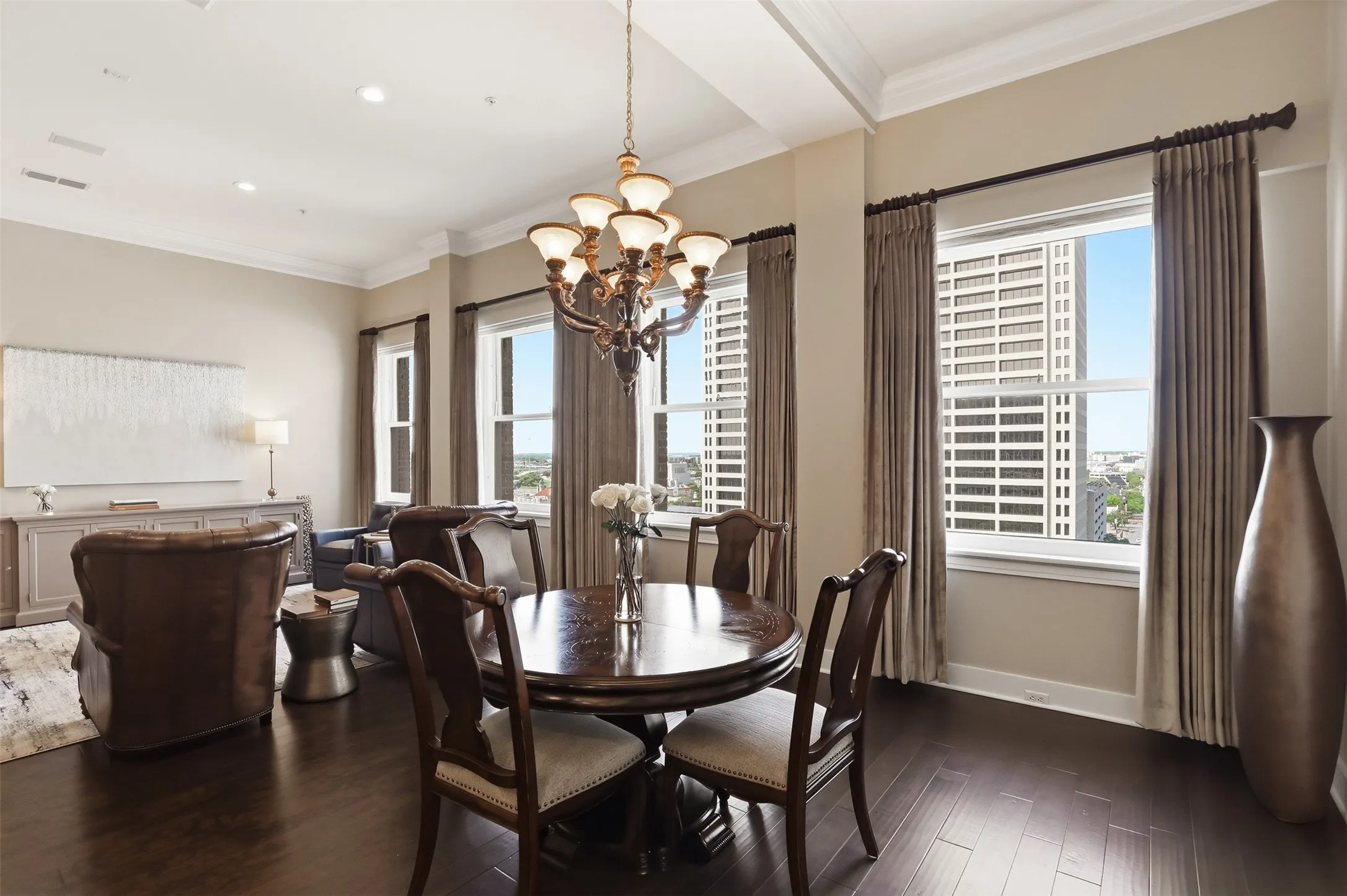 Dark wood-finish flooring with a decorative chandelier, crown molding, and large windows