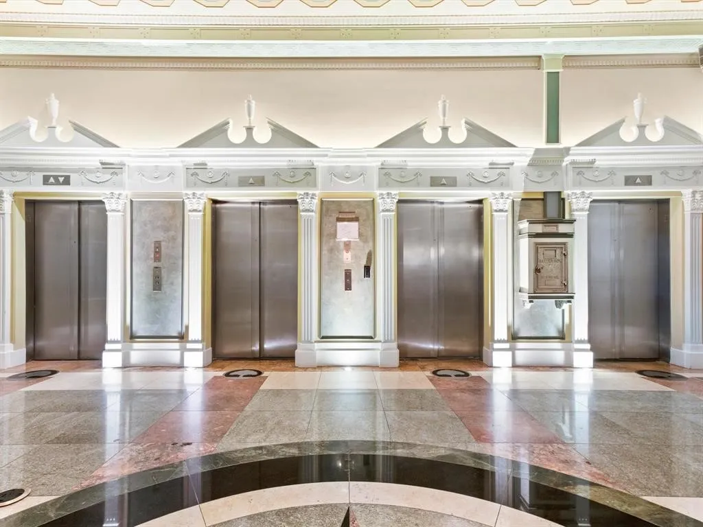 Historic Elevators in Stunning Neil P Lobby Polished stone flooring with intricate inlay, multiple elevator doors with stainless steel finishes, decorative architectural columns, and ornate ceiling trim