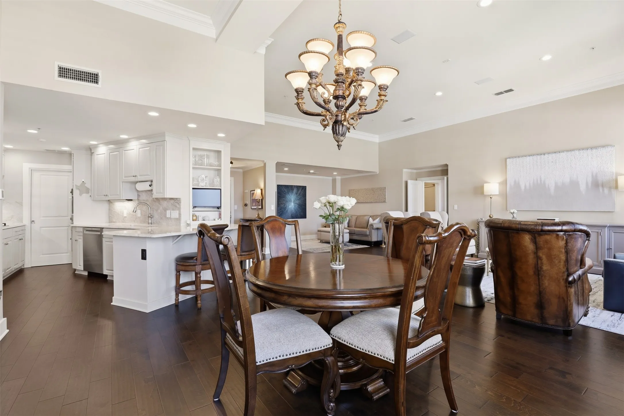Open-concept living area featuring dark wood-finish flooring, a kitchen with white cabinetry and stainless steel appliances, a kitchen island with seating, a dining area with an overhead chandelier, and recessed lighting