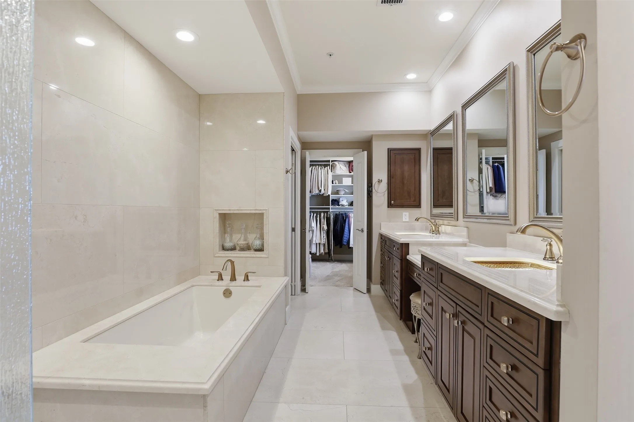 Built-in soaking tub with a tiled surround, dual vanity with undermount sinks, bronze finish fixtures, dark wood-finish cabinetry, and recessed lighting