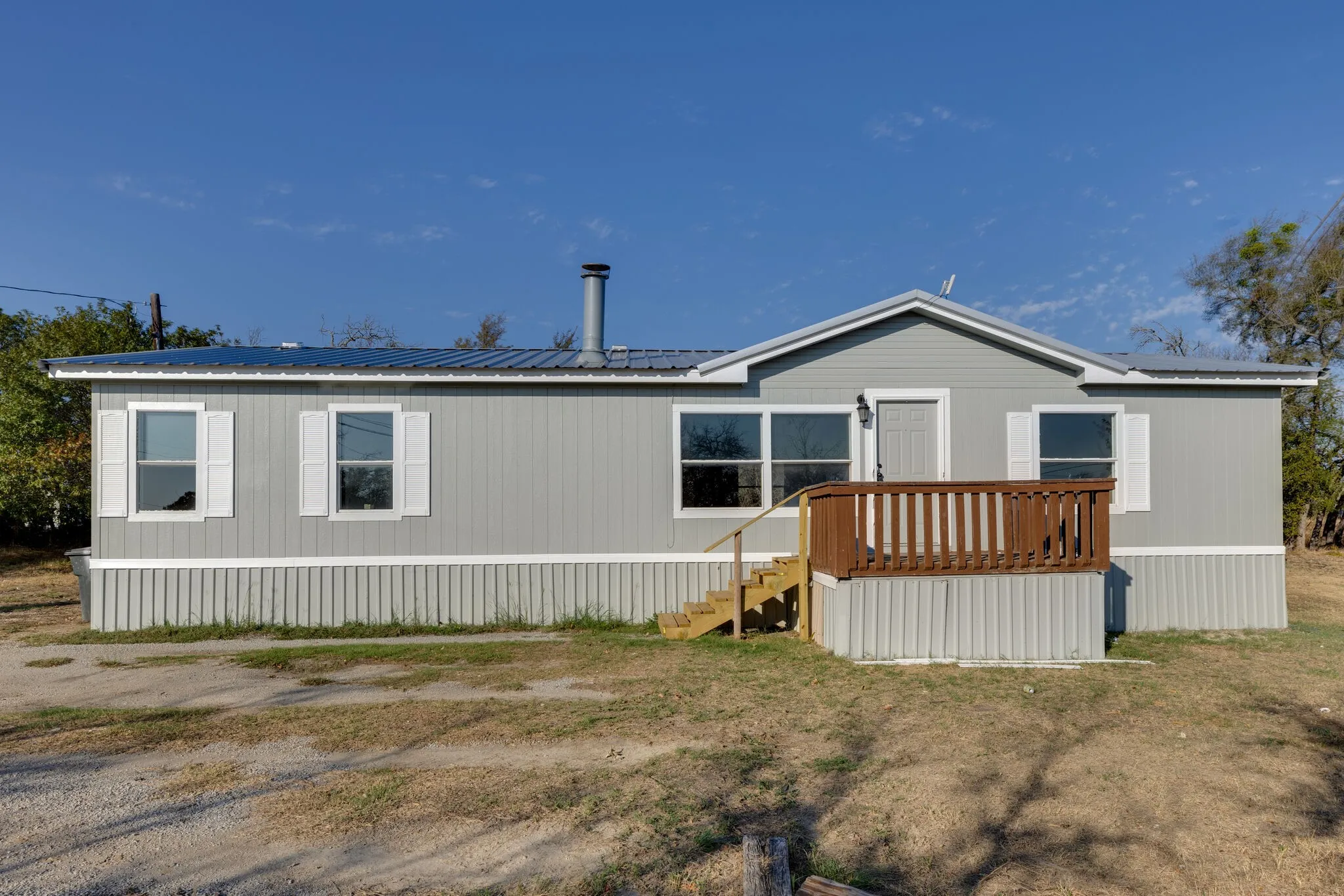 Light gray siding with white trim, metal roofing, white window shutters, and a wooden entry deck with steps