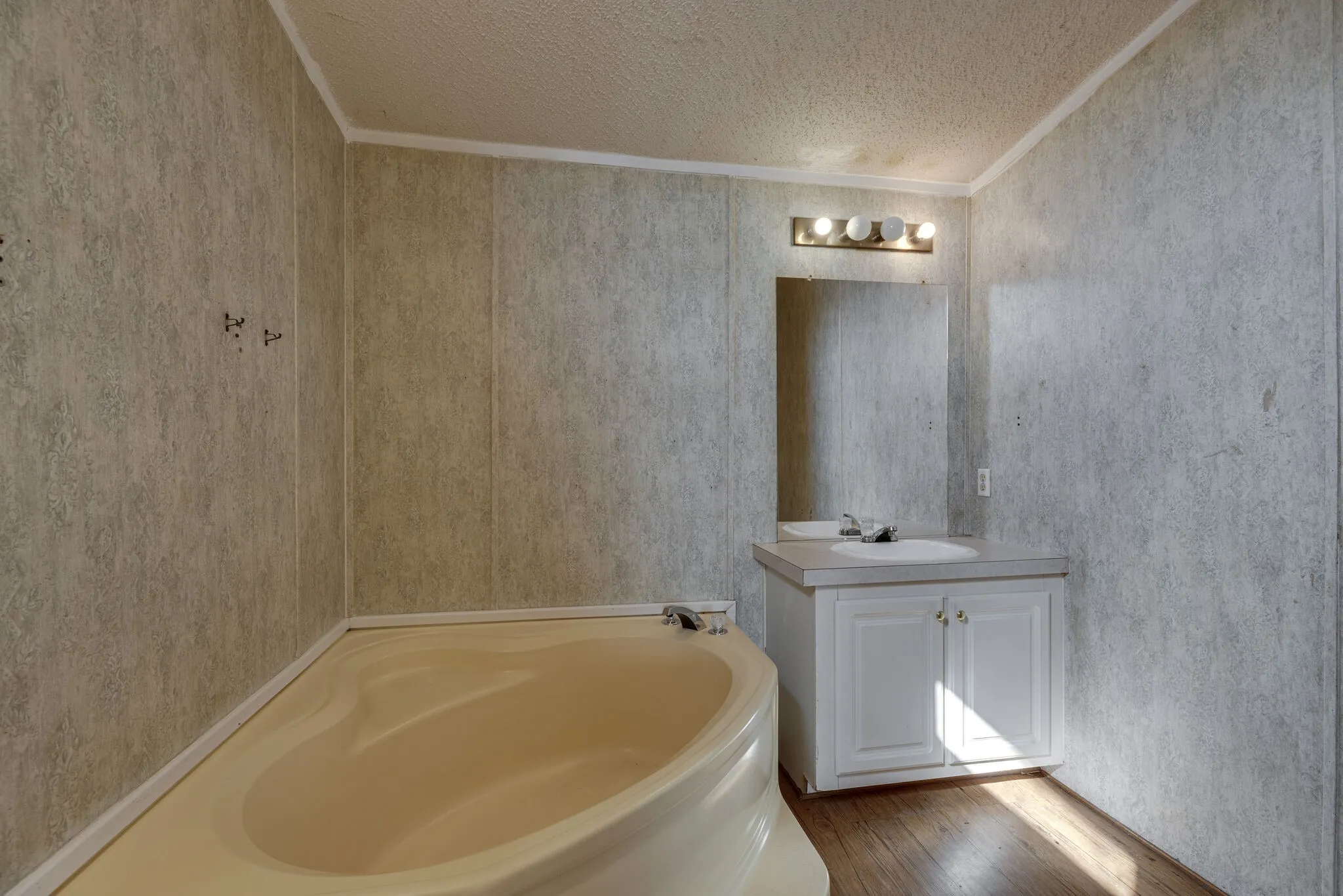 Corner bathtub, single vanity with white cabinetry, mirrored medicine cabinet, and wood-finish flooring