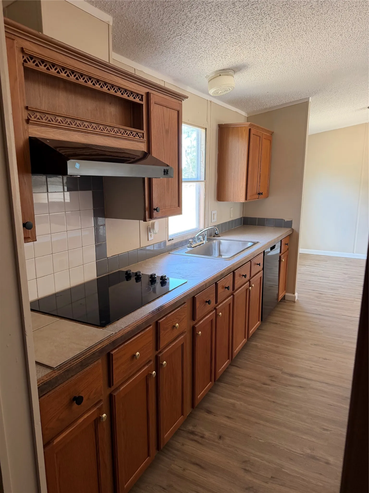 Well-appointed kitchen featuring wood-finish cabinetry, tile backsplash, built-in cooktop, stainless steel dishwasher, and wood-finish flooring