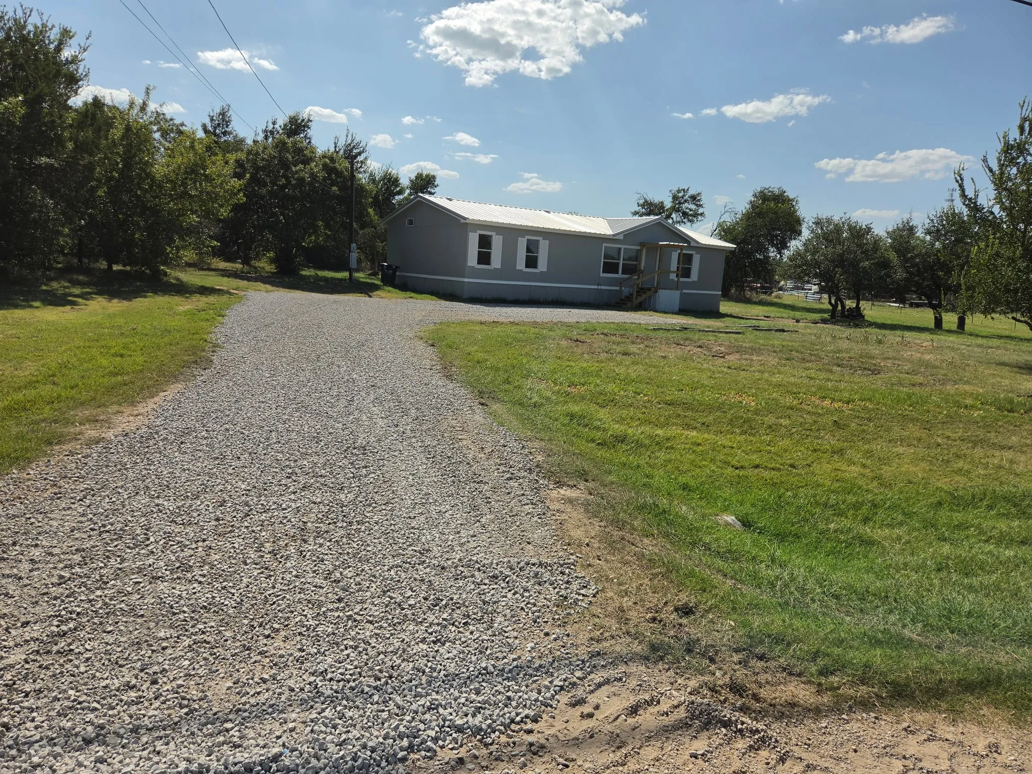 Gravel driveway leading to a single-story residence with gray siding and white trim