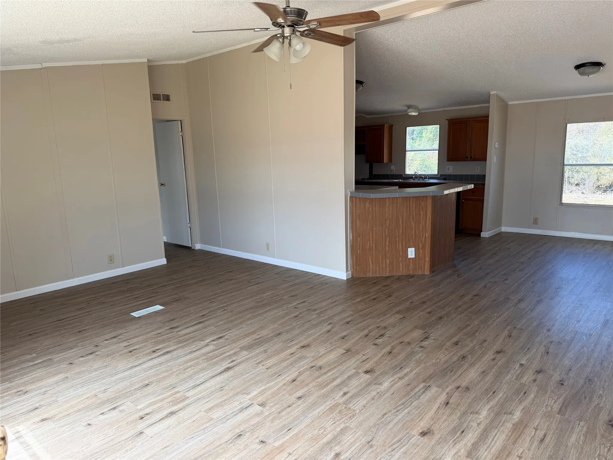 Open-concept living area with wood-finish flooring throughout, ceiling fan with brushed metal finish, and abundant natural light from multiple windows