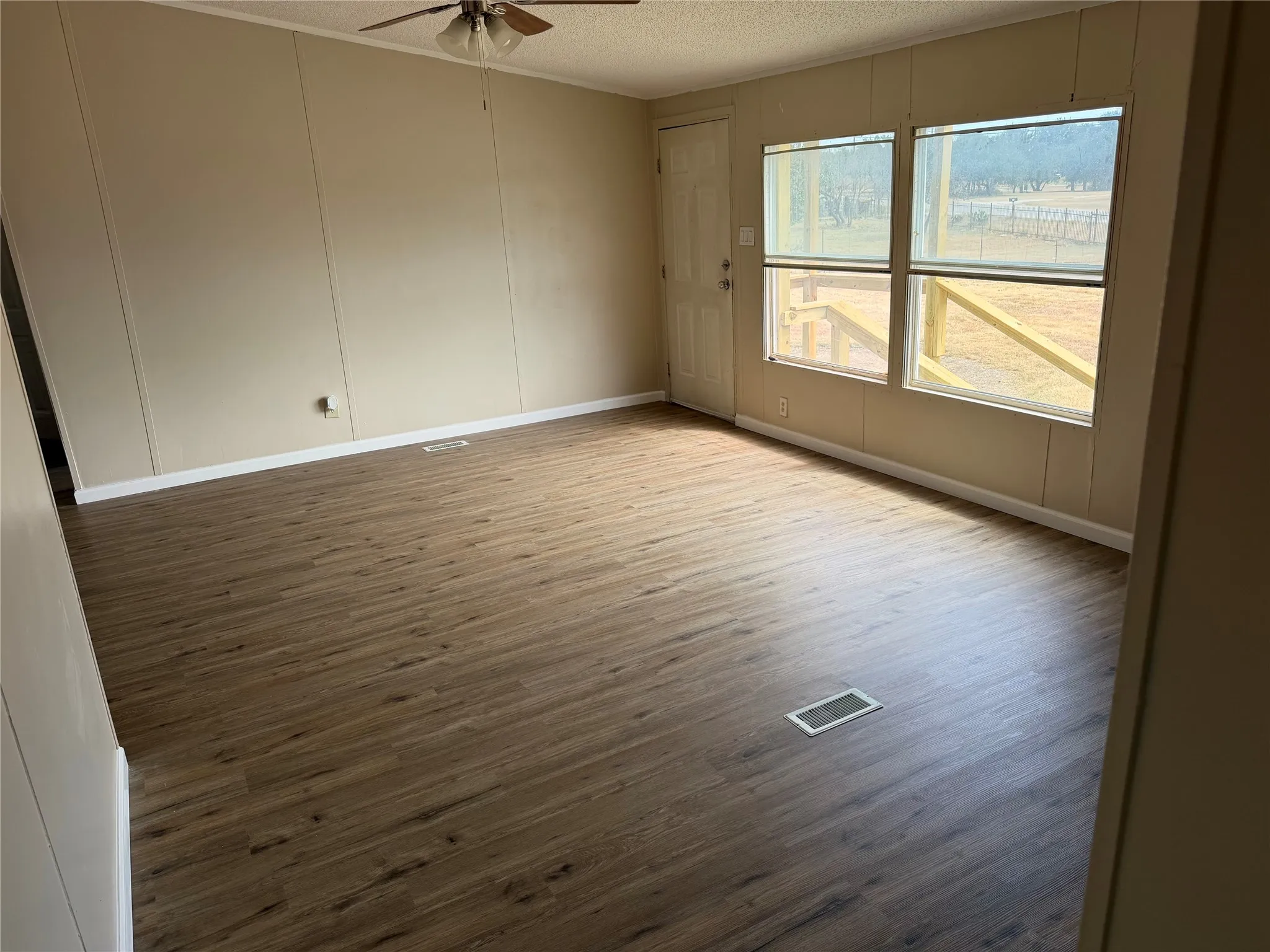 Spacious room featuring wood-finish flooring, two large windows, a ceiling fan, and a white paneled door