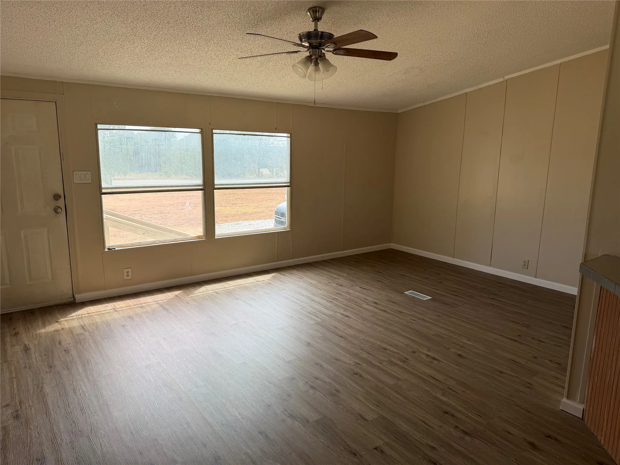 Spacious room featuring wood-finish flooring, ceiling fan with integrated lighting, large dual-pane windows with natural light exposure, and neutral wall finishes throughout