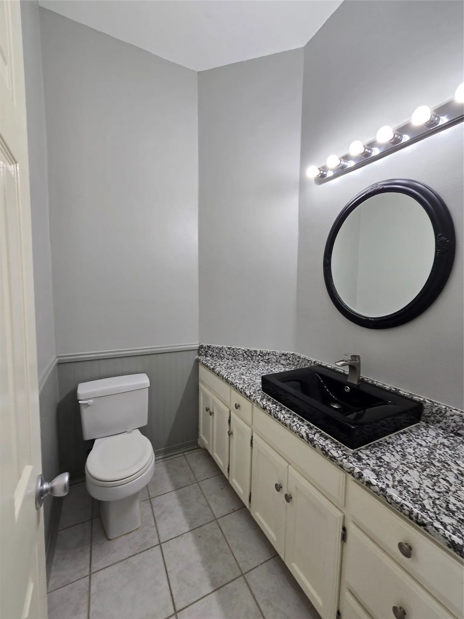 Vanity with a black vessel sink, a speckled countertop, and white cabinetry