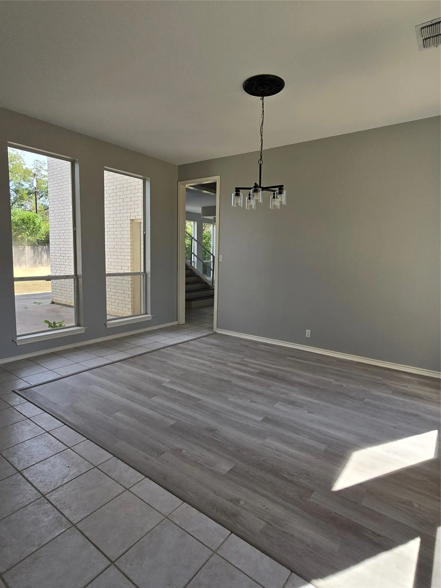 Spacious room featuring wood-finish flooring, a contemporary chandelier, and large windows