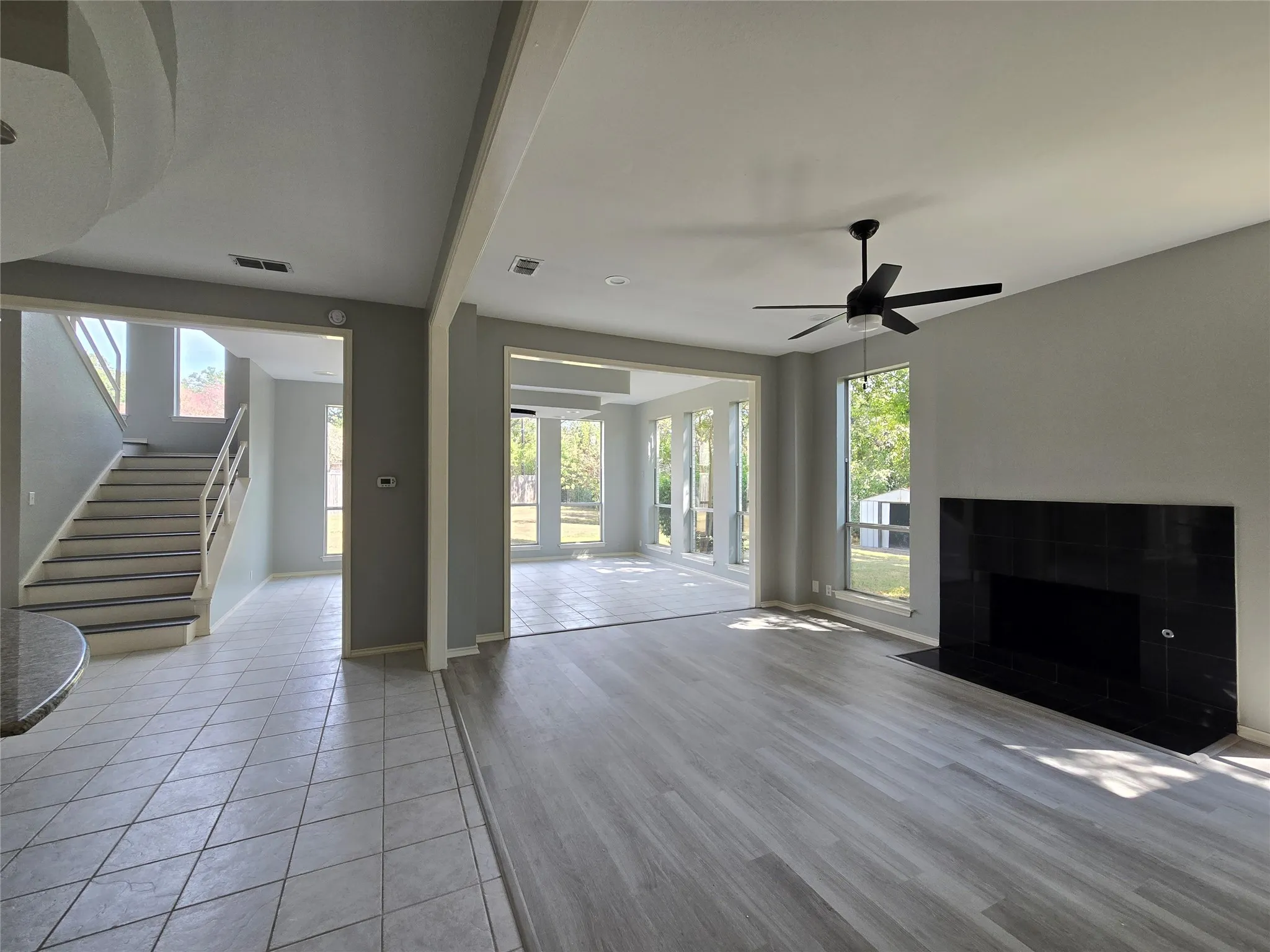 Black stone fireplace, wood-finish flooring, staircase with white railing, ceiling fan, and tiled entry