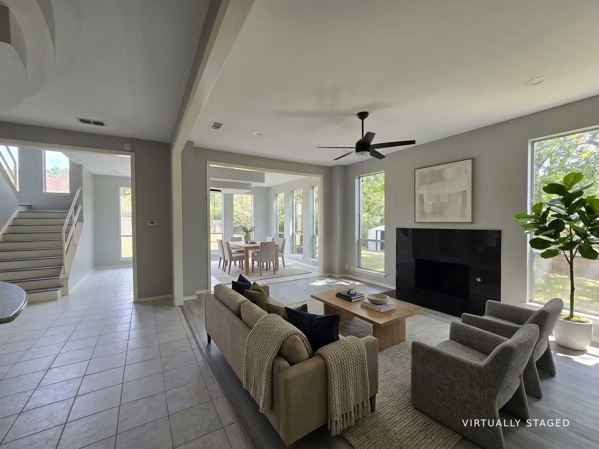 Spacious living area featuring large windows, a sleek black fireplace, and a ceiling fan