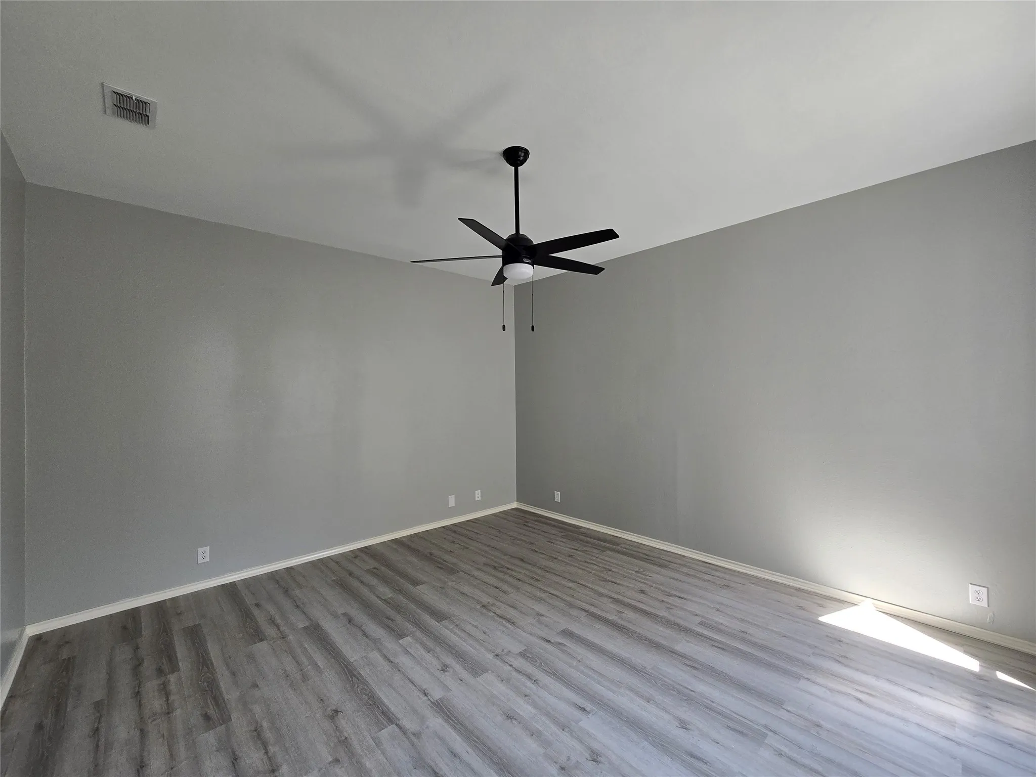 Wood-finish flooring with a light gray tone, ceiling fan with integrated lighting, and neutral gray wall paint