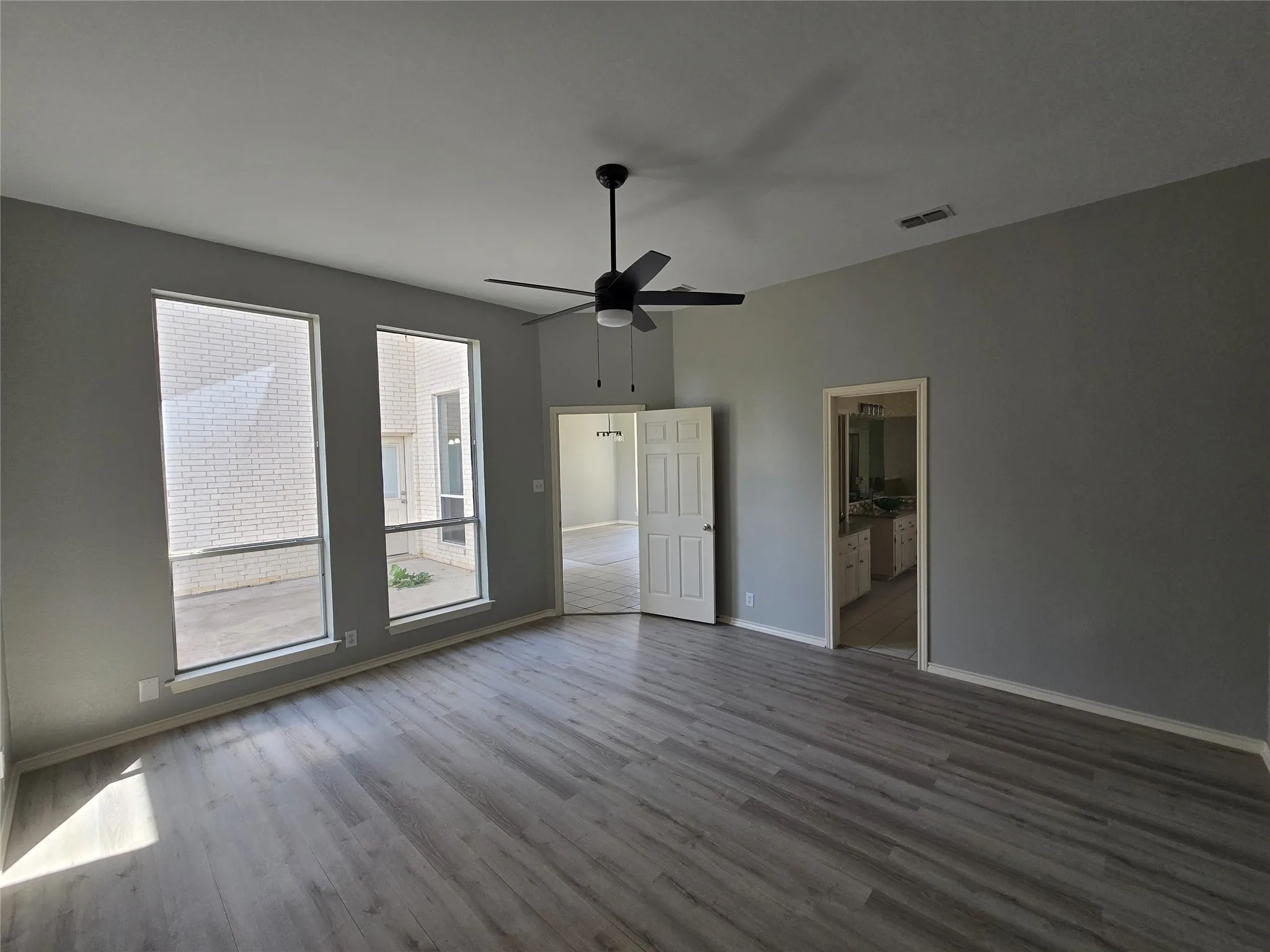 Vaulted ceiling with a ceiling fan, wood-finish flooring, two tall windows, and a white interior door
