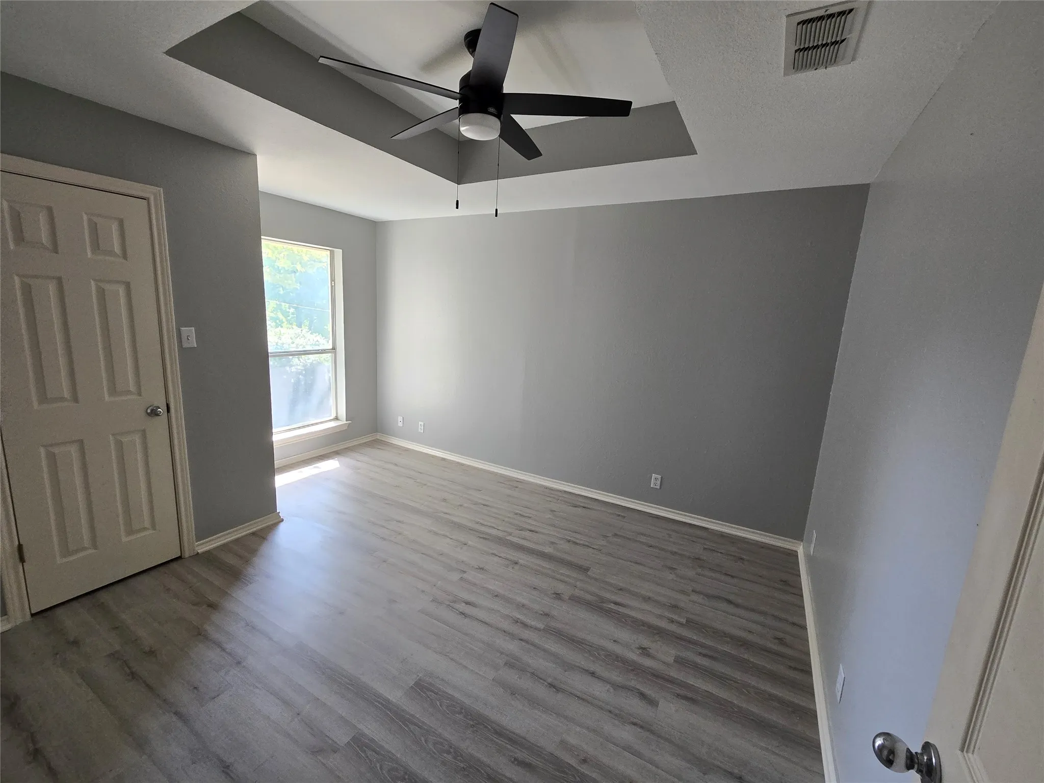 Recessed ceiling with a built-in ceiling fan, wood-finish flooring, and neutral wall paint