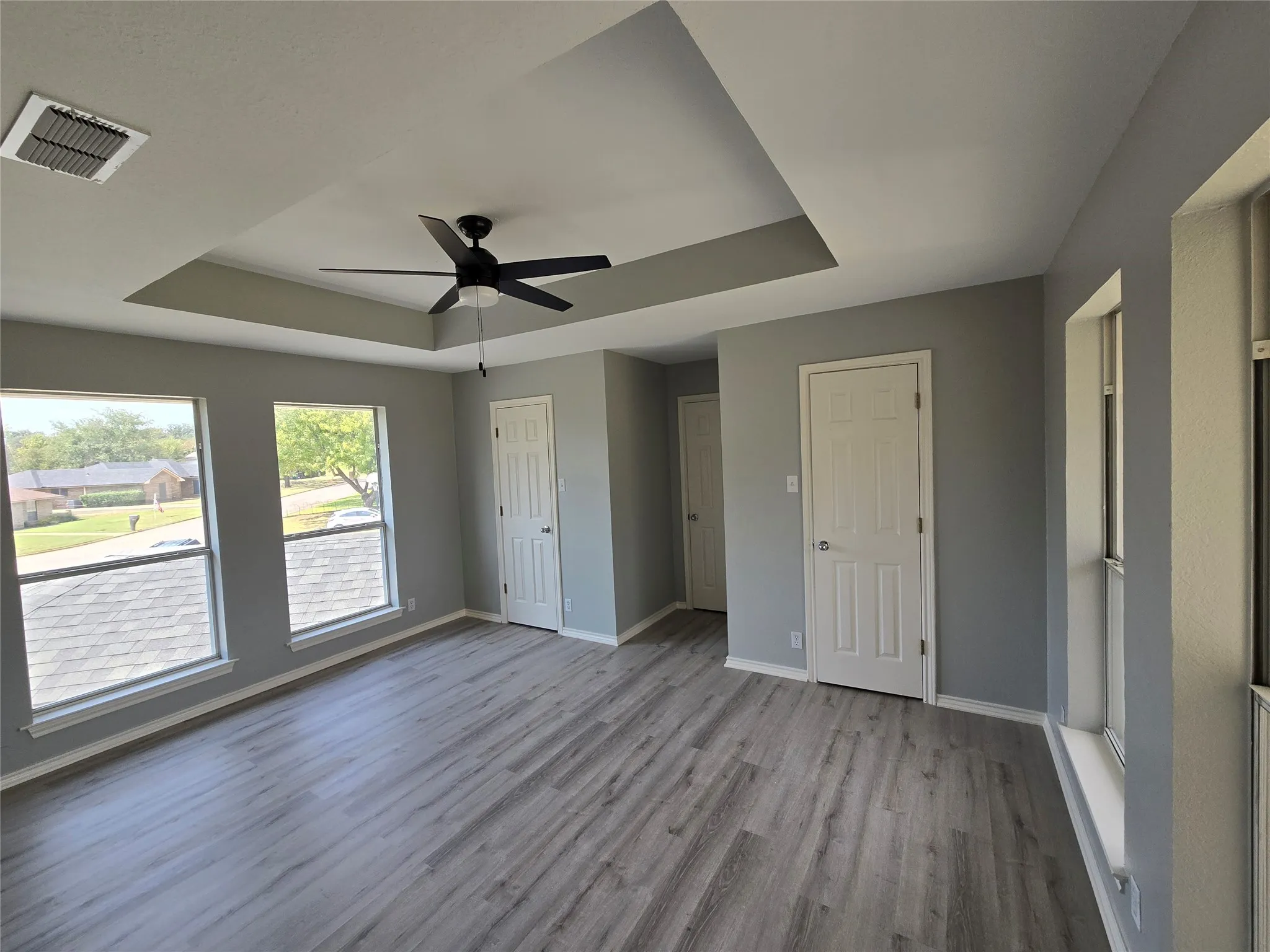 Tray ceiling with a ceiling fan, multiple windows, wood-finish flooring, and white paneled doors