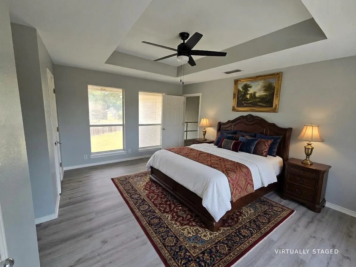 Tray ceiling, ceiling fan, two windows, wood-finish flooring, and white trim