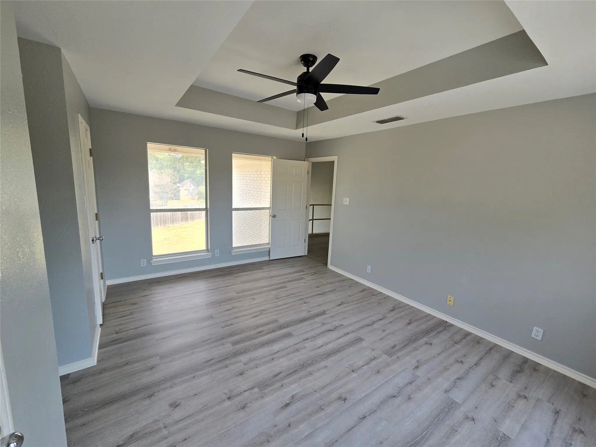 Recessed ceiling, ceiling fan, two windows, two doors, wood-finish flooring