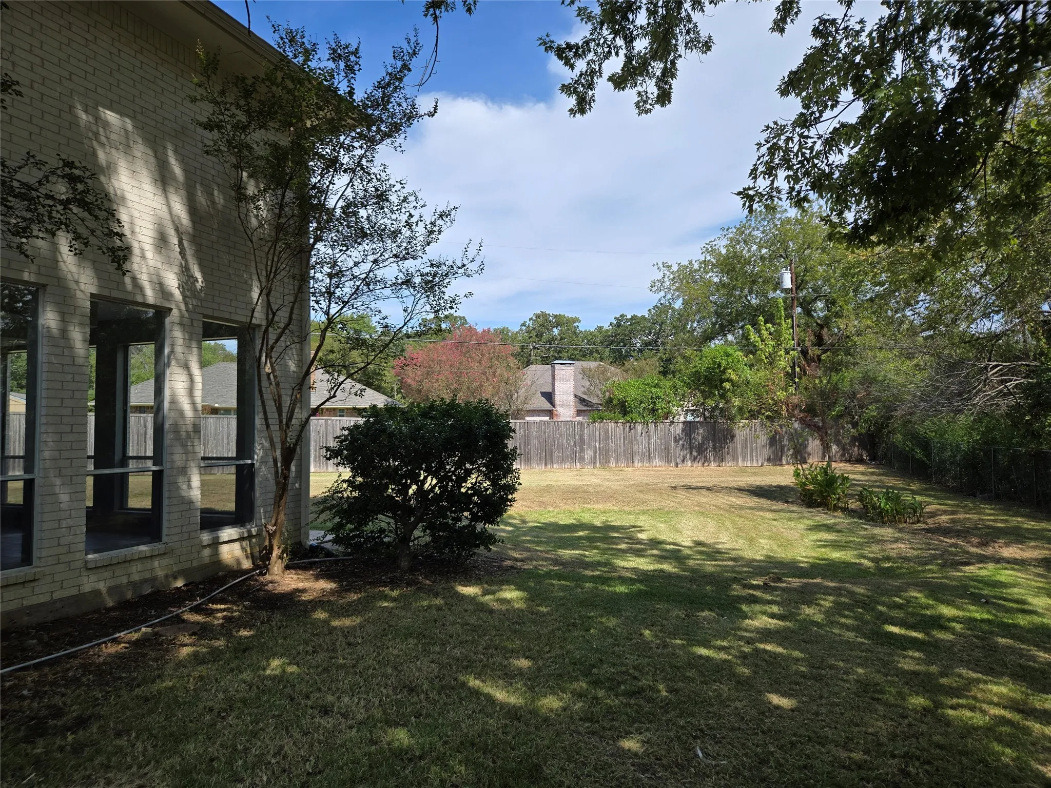 Expansive backyard featuring a manicured lawn, established trees, and a privacy fence