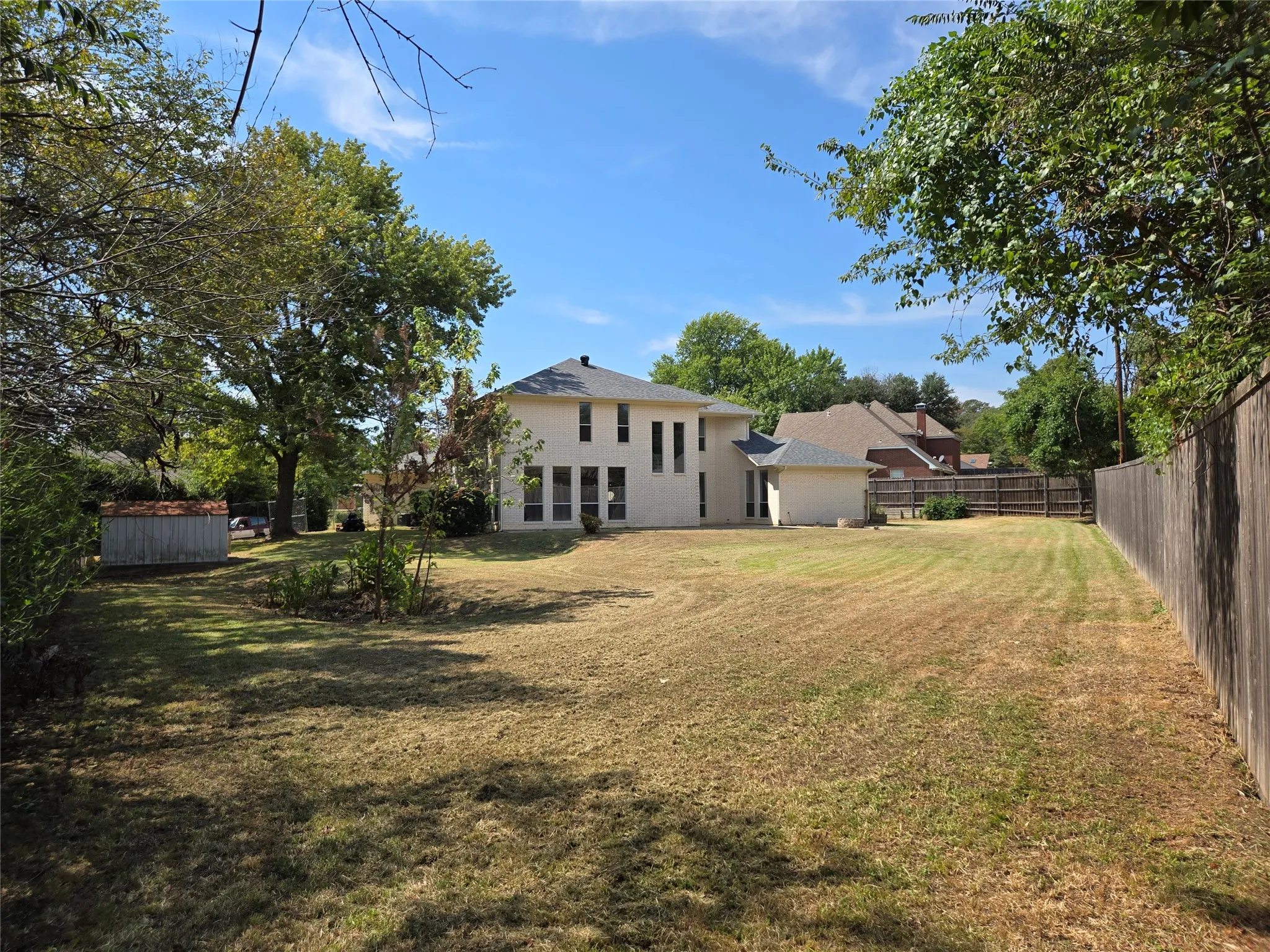 Expansive rear yard with a two-story exterior, multiple windows, a detached storage shed, and a privacy fence